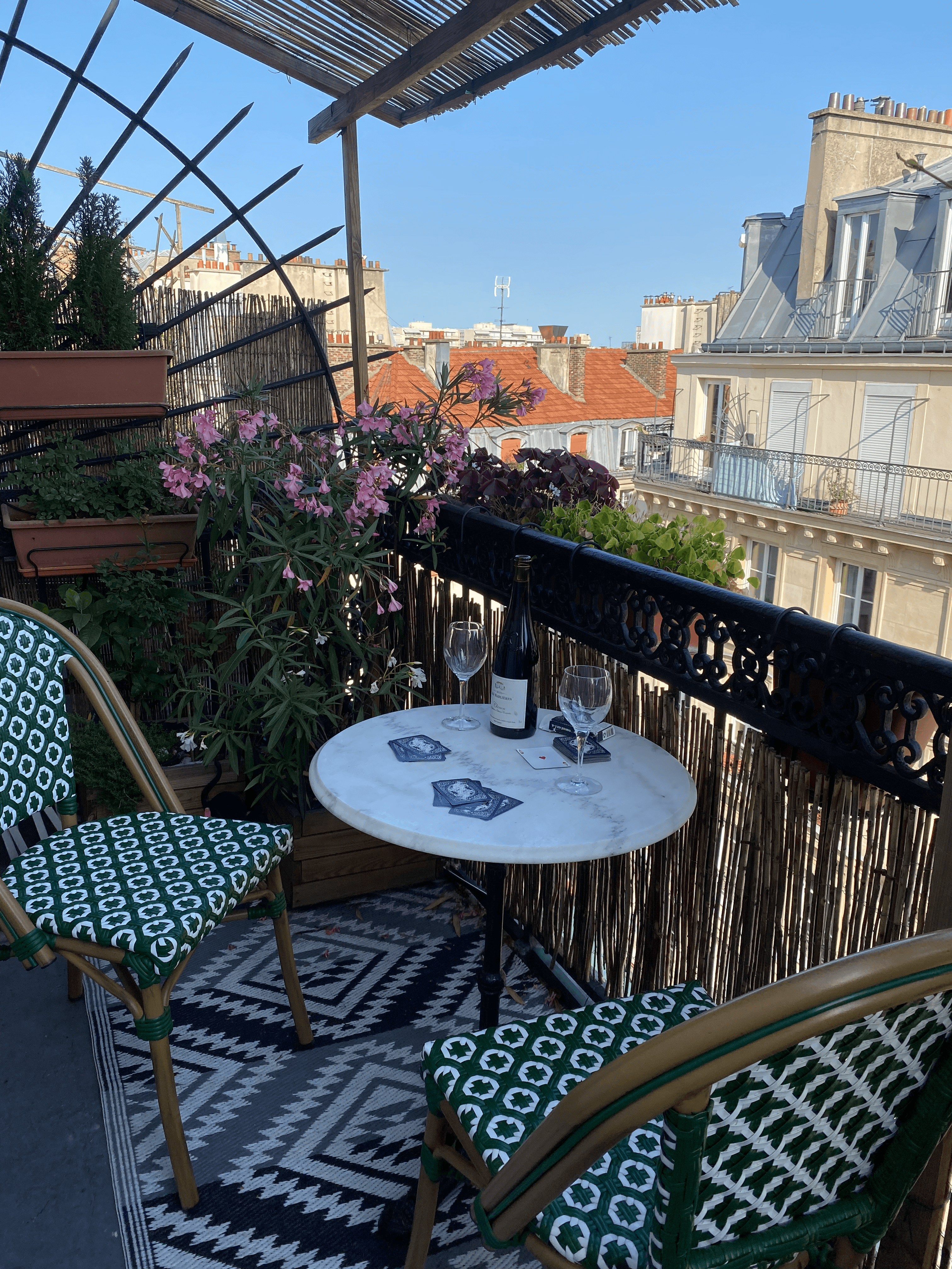 View of a round marble table with wine glasses and two chairs on a balcony overlooking rooftops on a sunny day