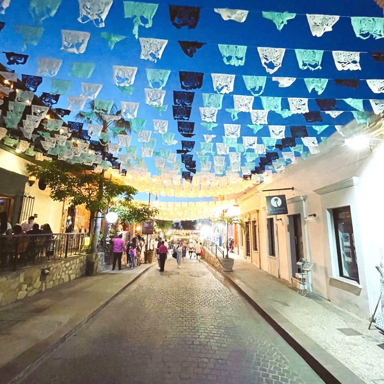 View of a street with small blue and white flags hanging above at sundown