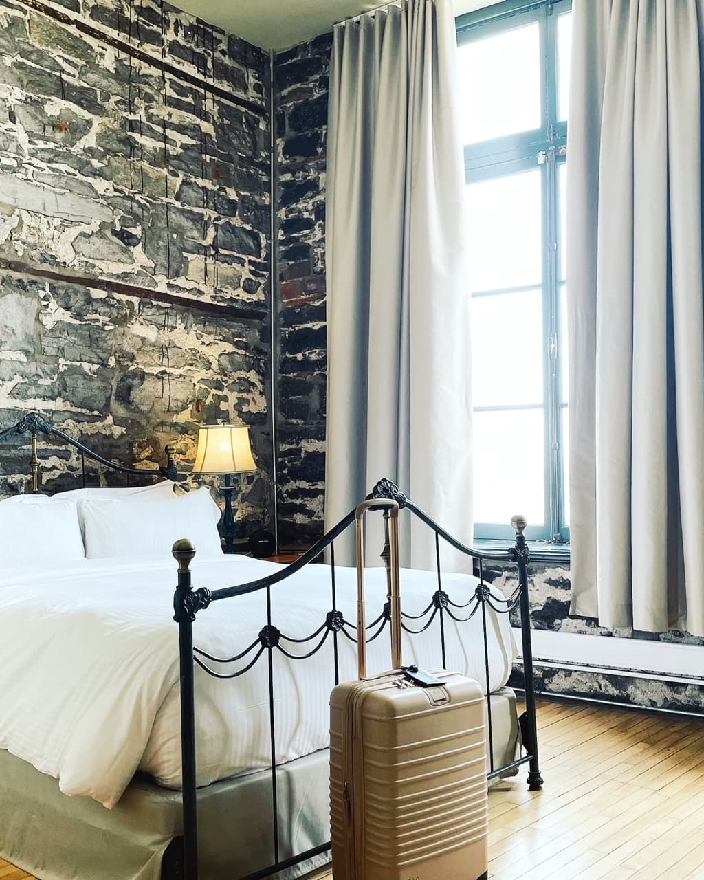 View of a beautiful hotel room with exposed stone walls and floor to ceiling windows with sunlight streaming in