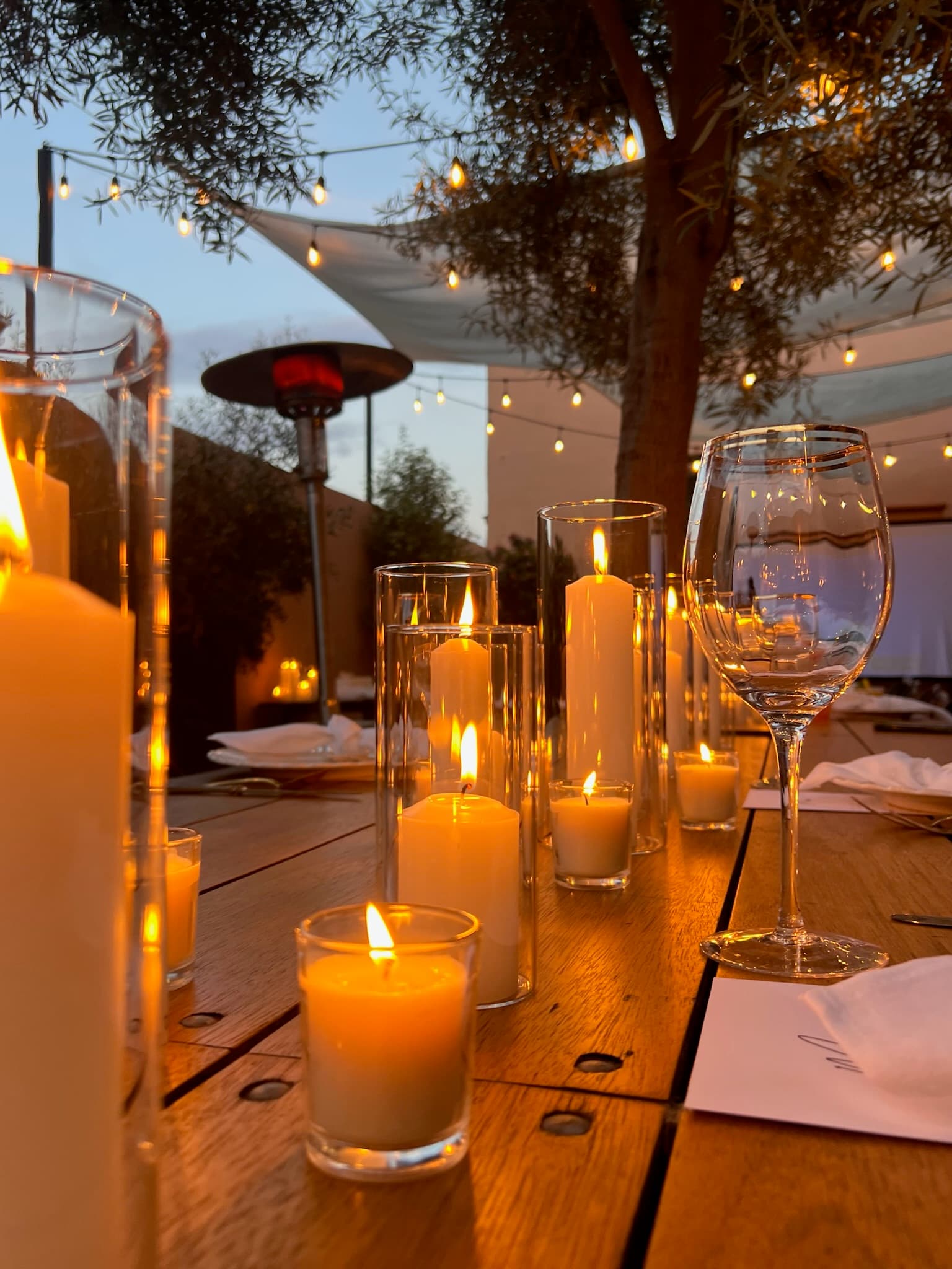 A candlelit table under a canopy covered in twinkle lights at dusk.