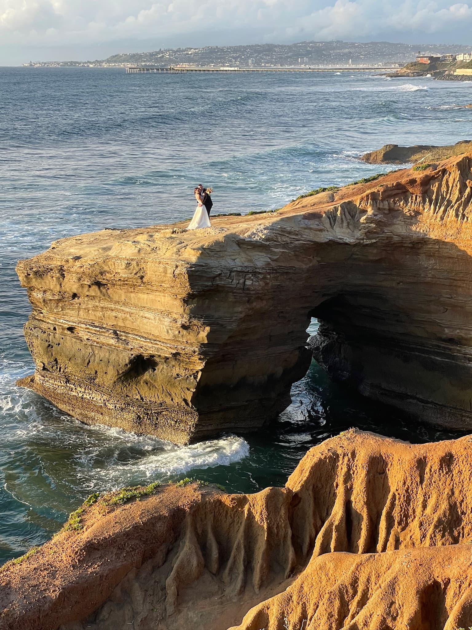 Advisor posing on the edge of a cliffside as waves lap the craggy shore under a cloudy daytime sky. 