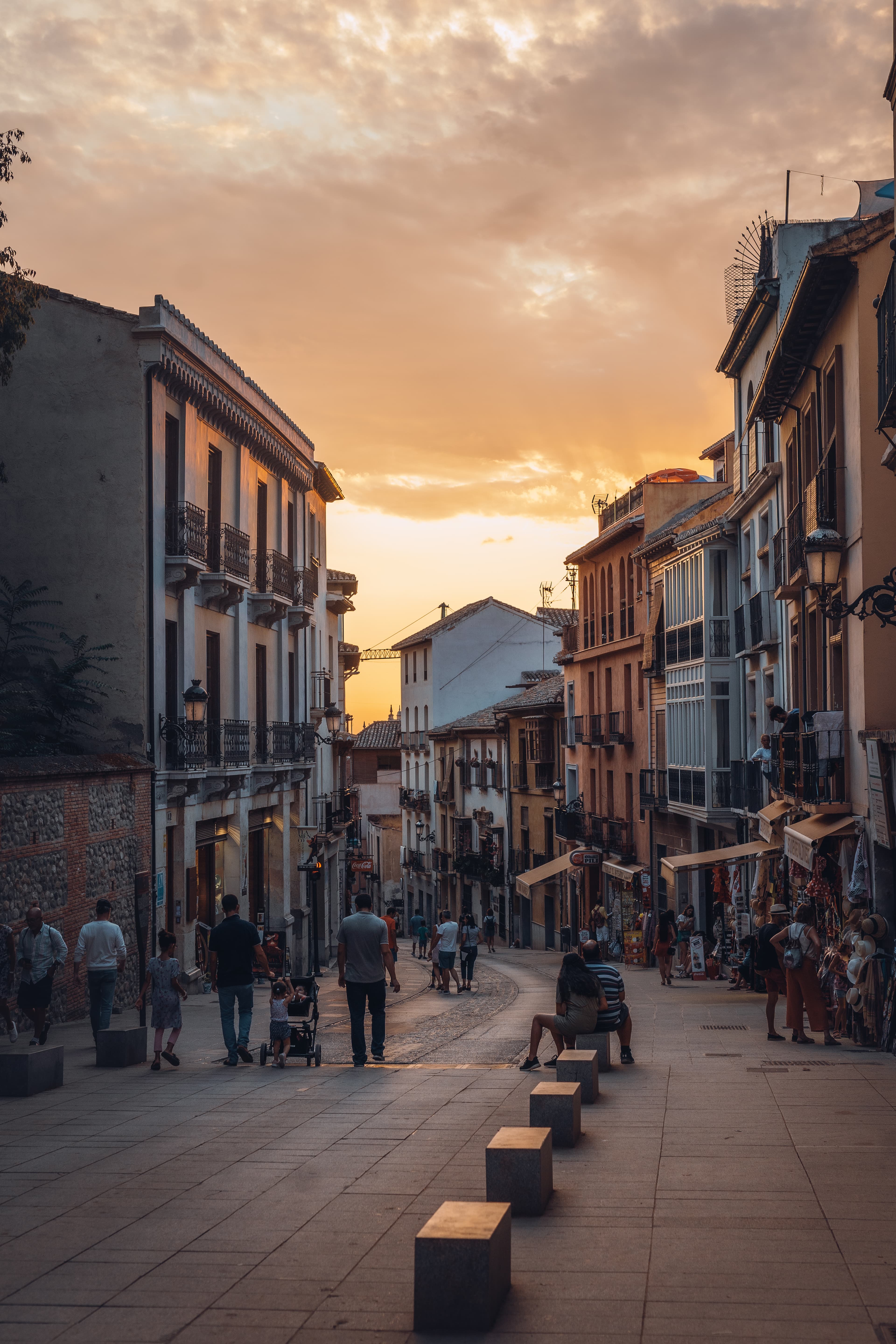 Tourists mill below quaint city buildings that wind along a street under a pink sky at dusk. 