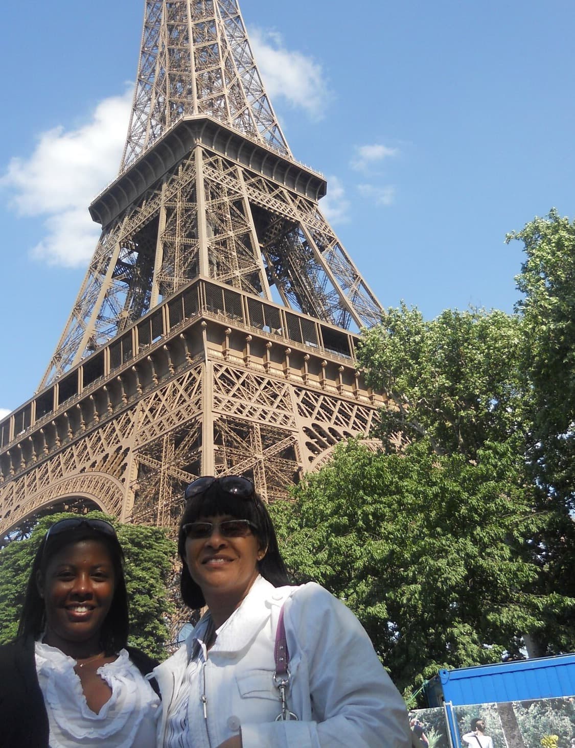 Two people stand at the base of the Eiffel Tower during the daytime.