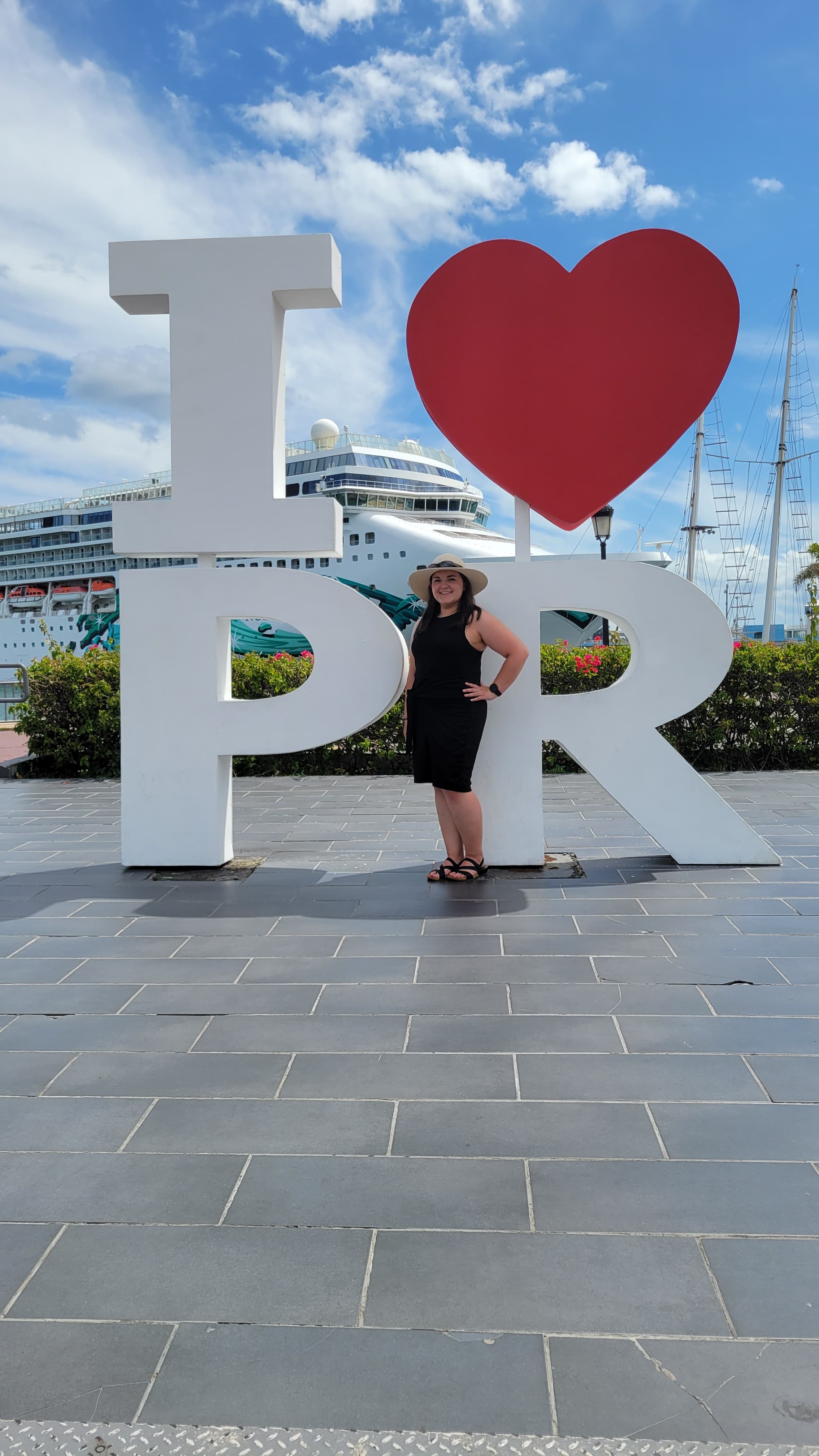 View of Kelli with her hand on her hip posing in front of a large sign reading “I <3 PR” on a sunny day