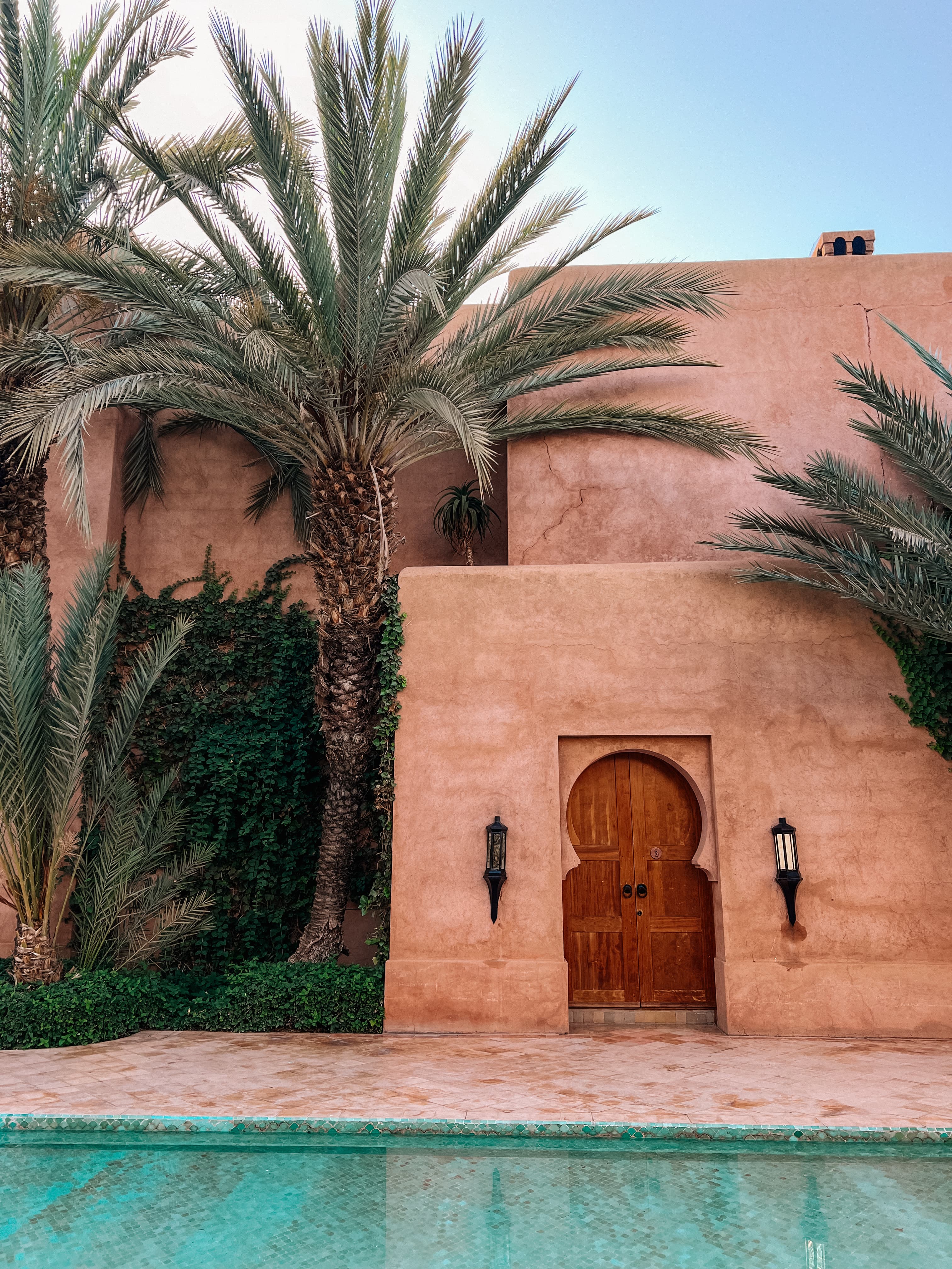 View of part of a pretty hotel pool near terracotta colored buildings and several palm trees