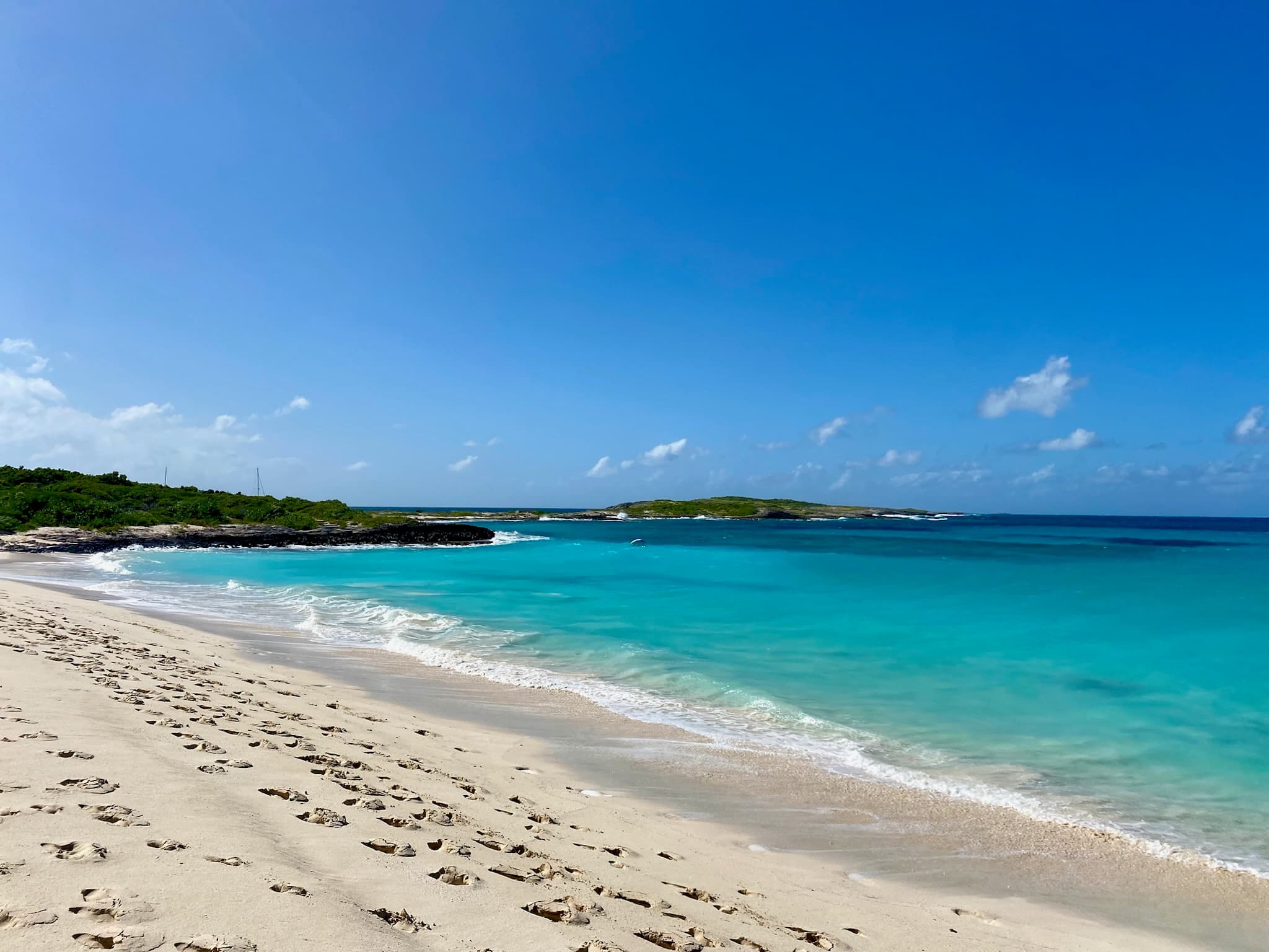 Beautiful view of a bright turquoise ocean besides a clean white sandy beach with footsteps in the sand on a sunny day