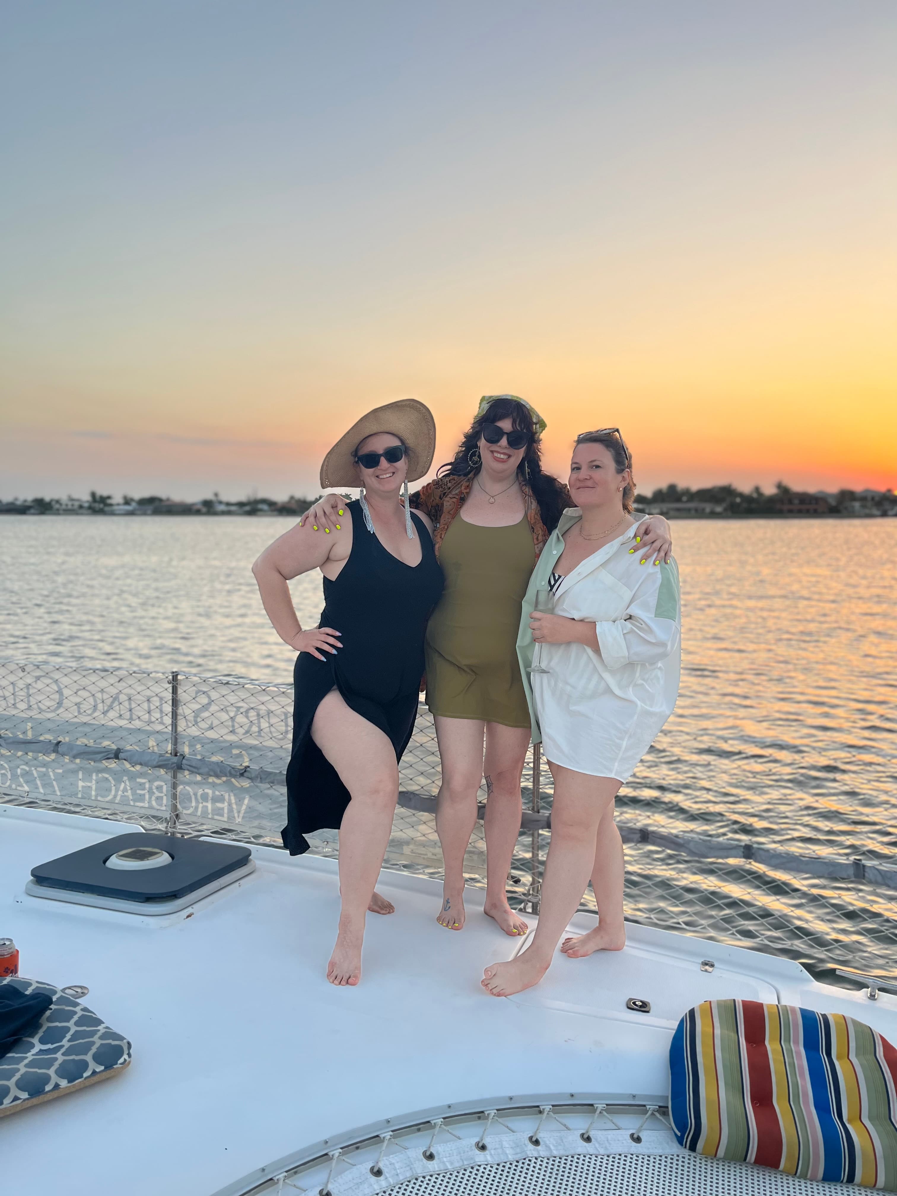 Three friends posing together on top of a boat during sunset.