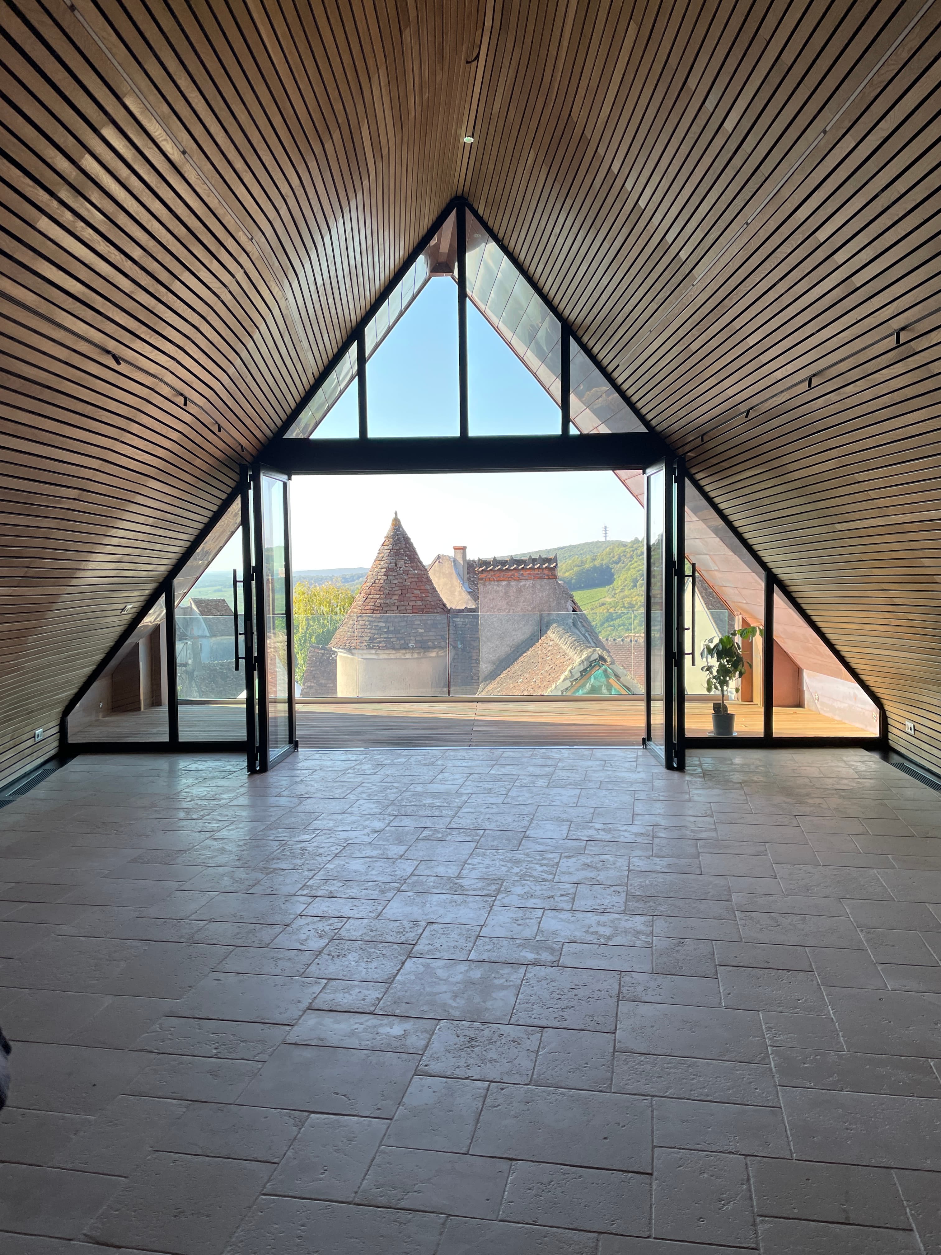 View from indoors of a pyramid-shaped roof and glass windows overlooking a green valley on a sunny day