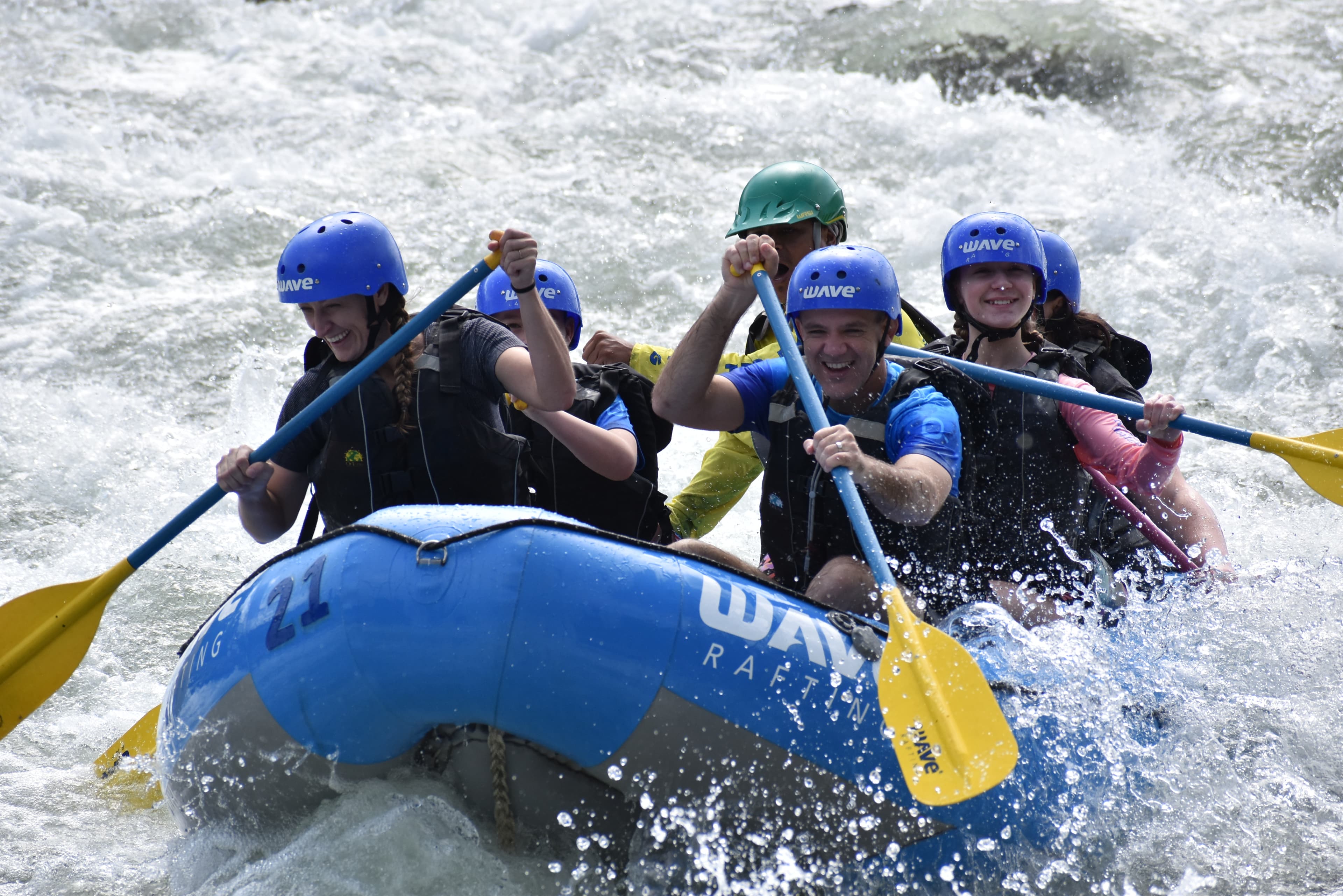 Brie and others white water rafting with blue helmets and yellow oars