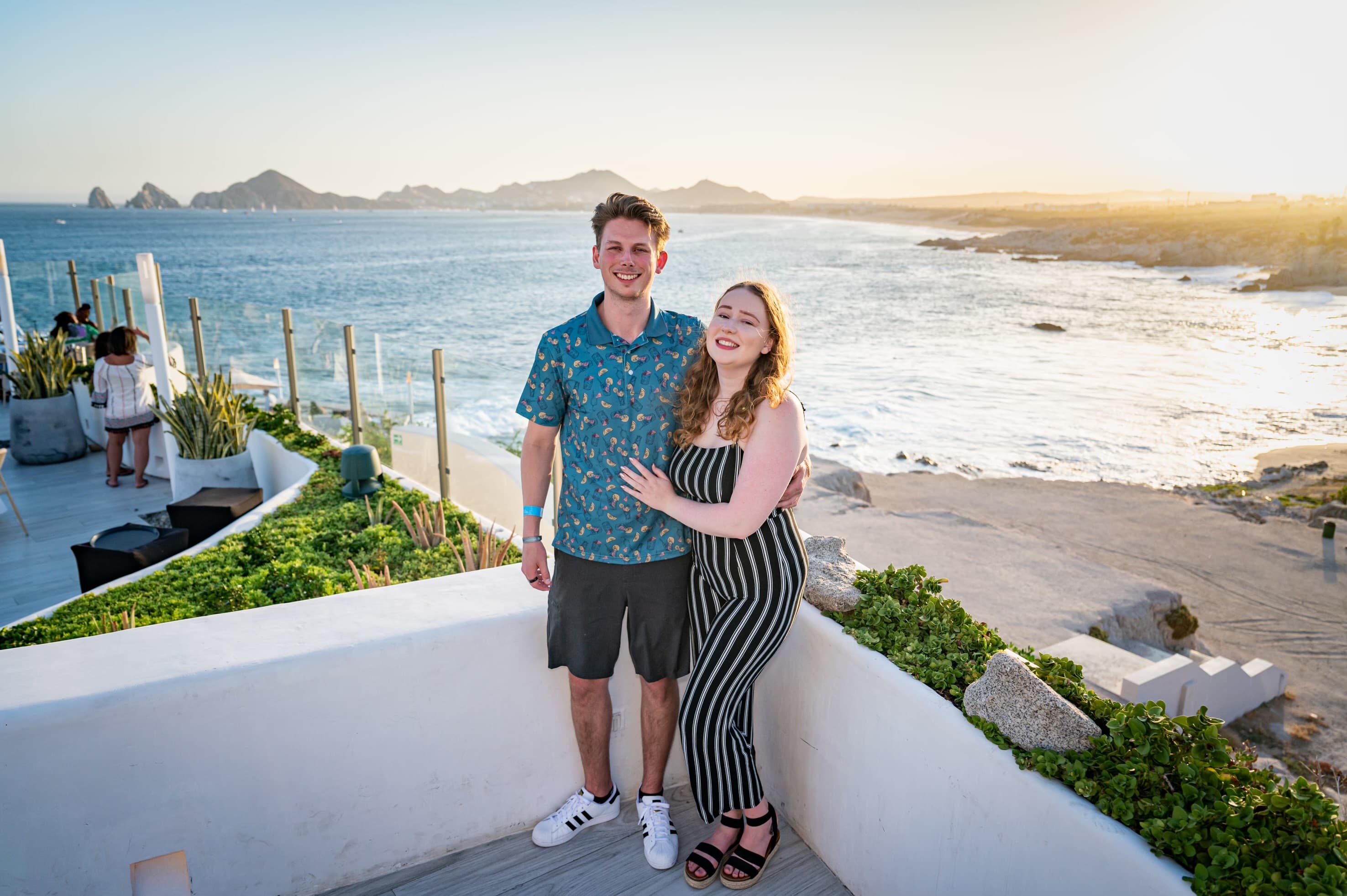 Advisor posing with partner in a black and white striped romper with the beach in the background.