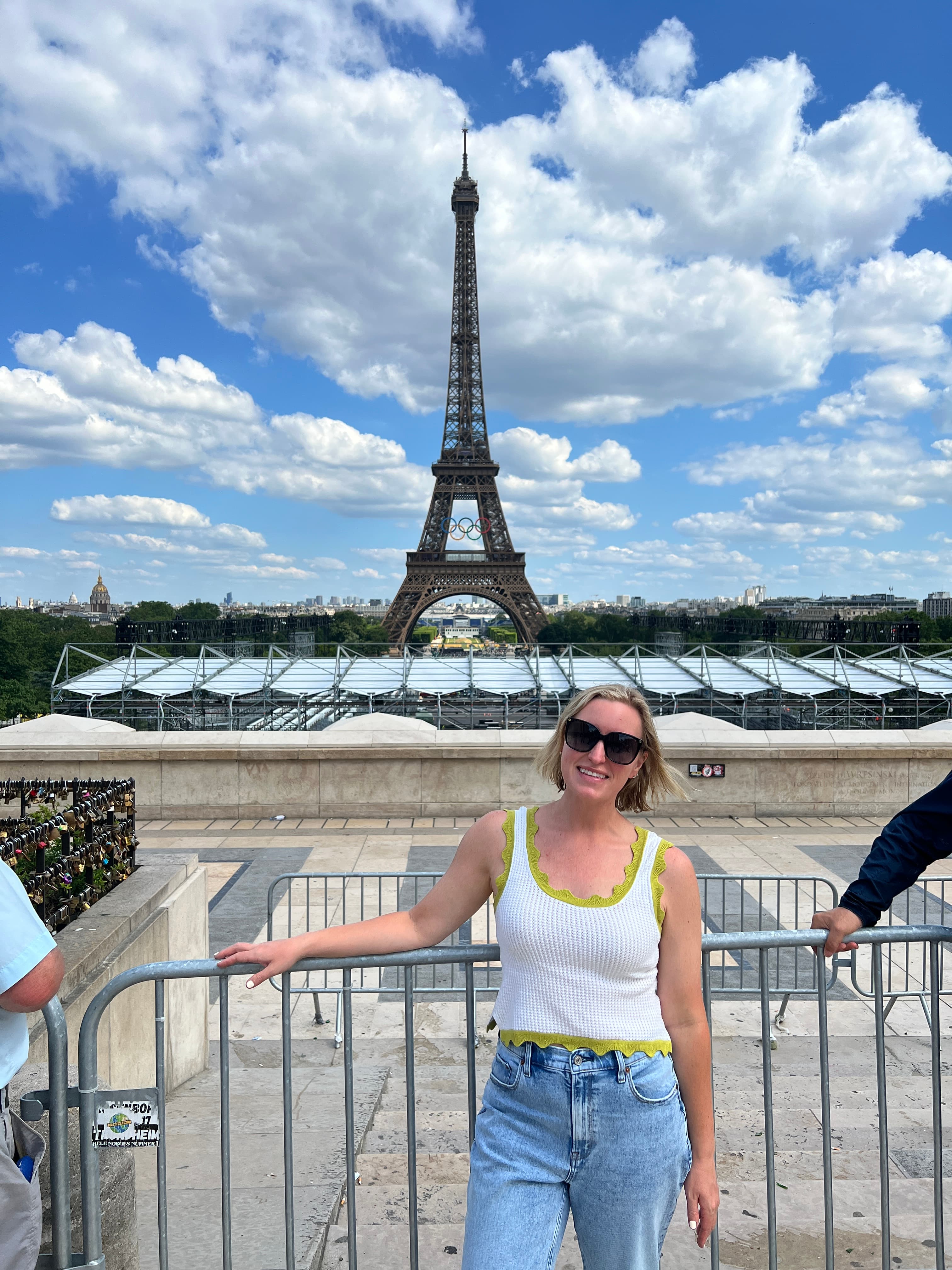 Amanda posing by a metal gate with the Eiffel Tower visible behind her on a sunny day