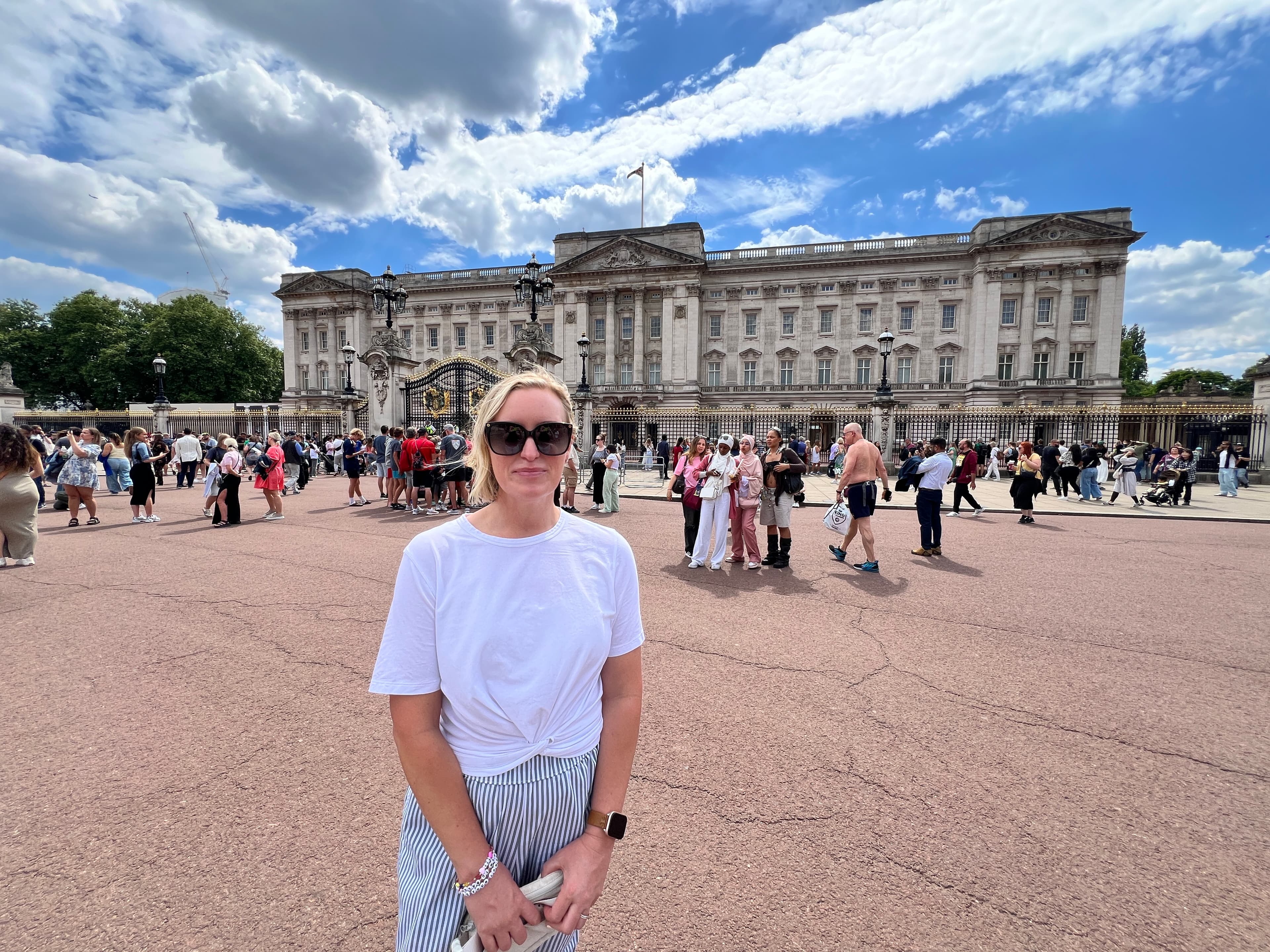 Amanda in a white t-shirt in front of a grand palace surrounded by visitors on a sunny day