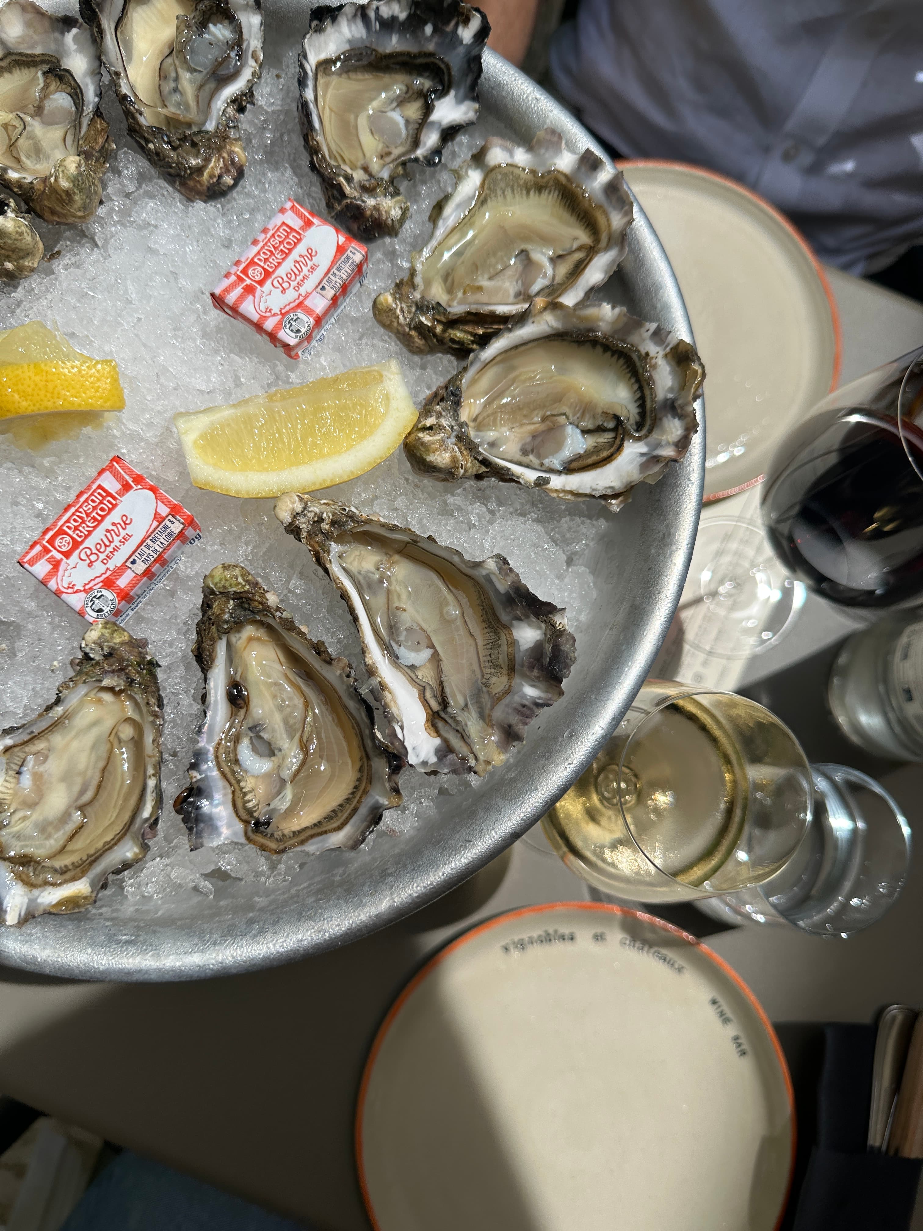 Overhead view of a tray of oysters on ice with lemon on a table with a glass of white wine