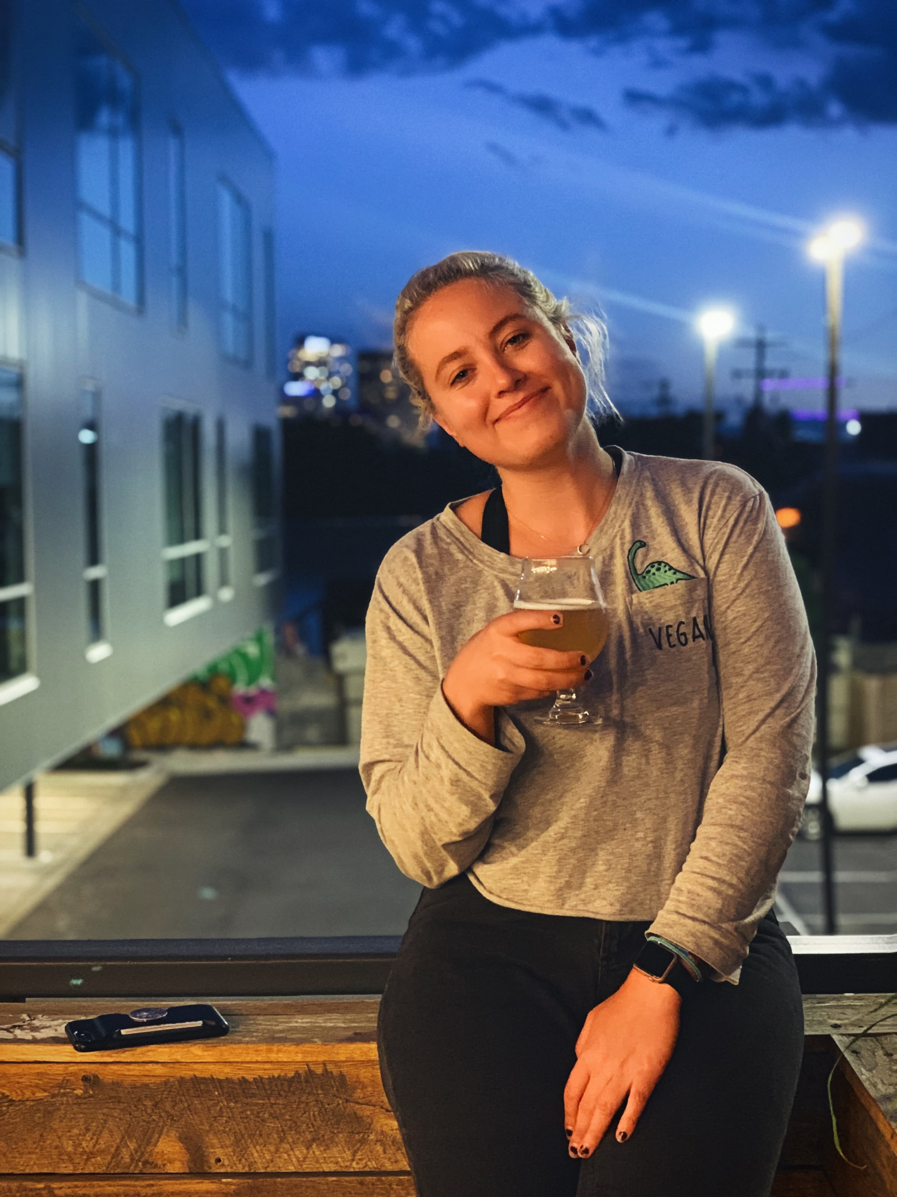 Jenna sitting on a window ledge holding a glass of beer at night