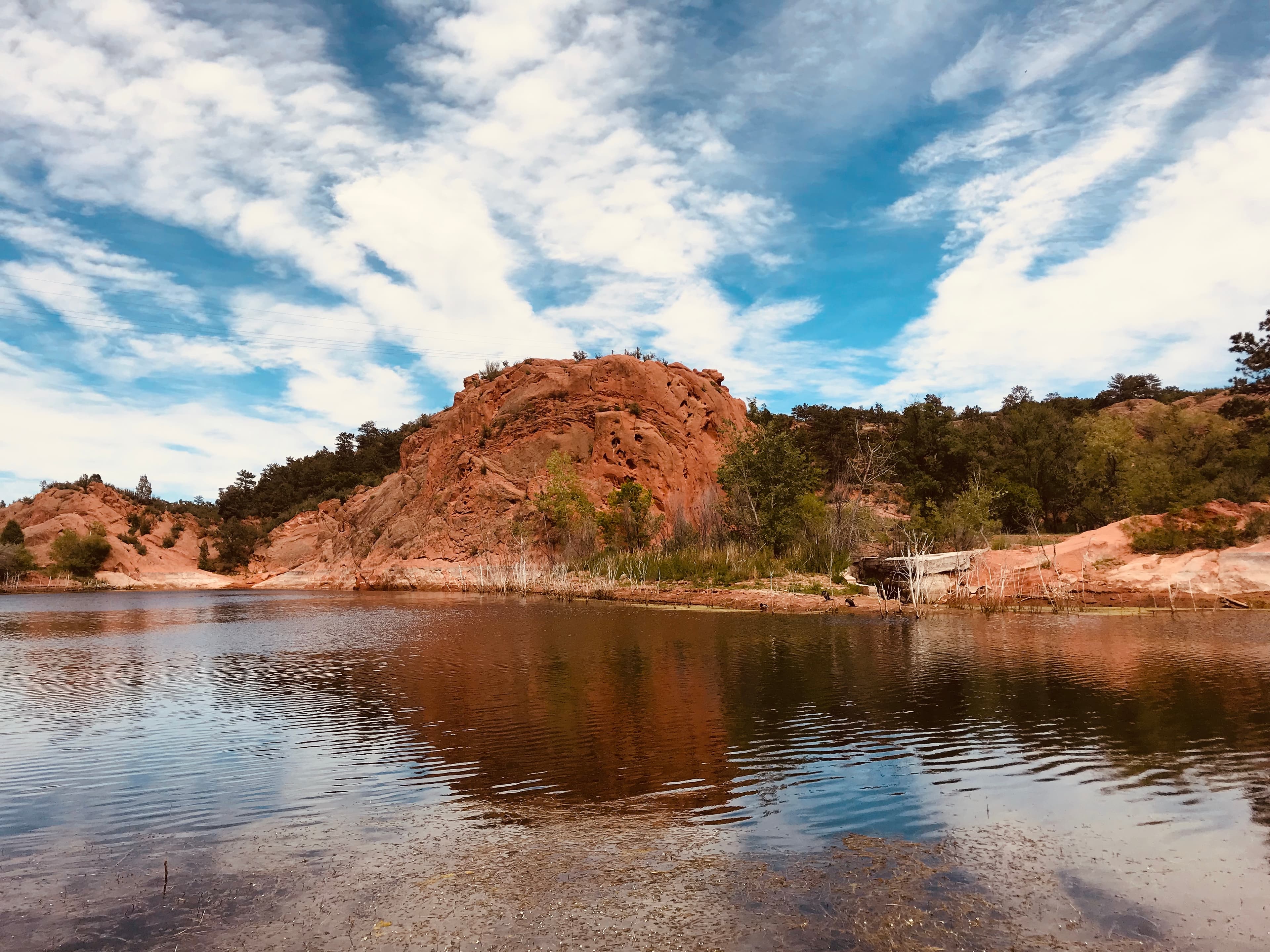 Beautiful view of a lake and red rock landscape with some trees under sunny skies