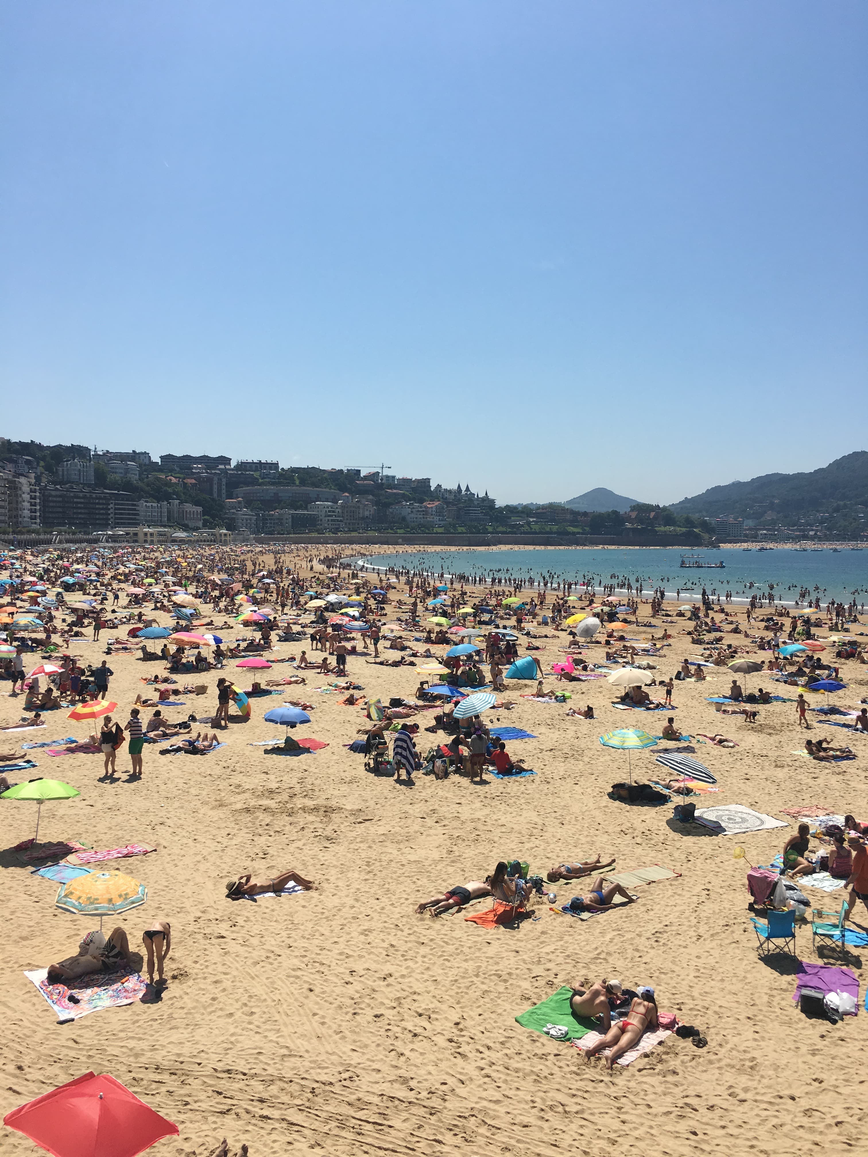 View of a beach, the sand crowded with sunbathers under clear skies