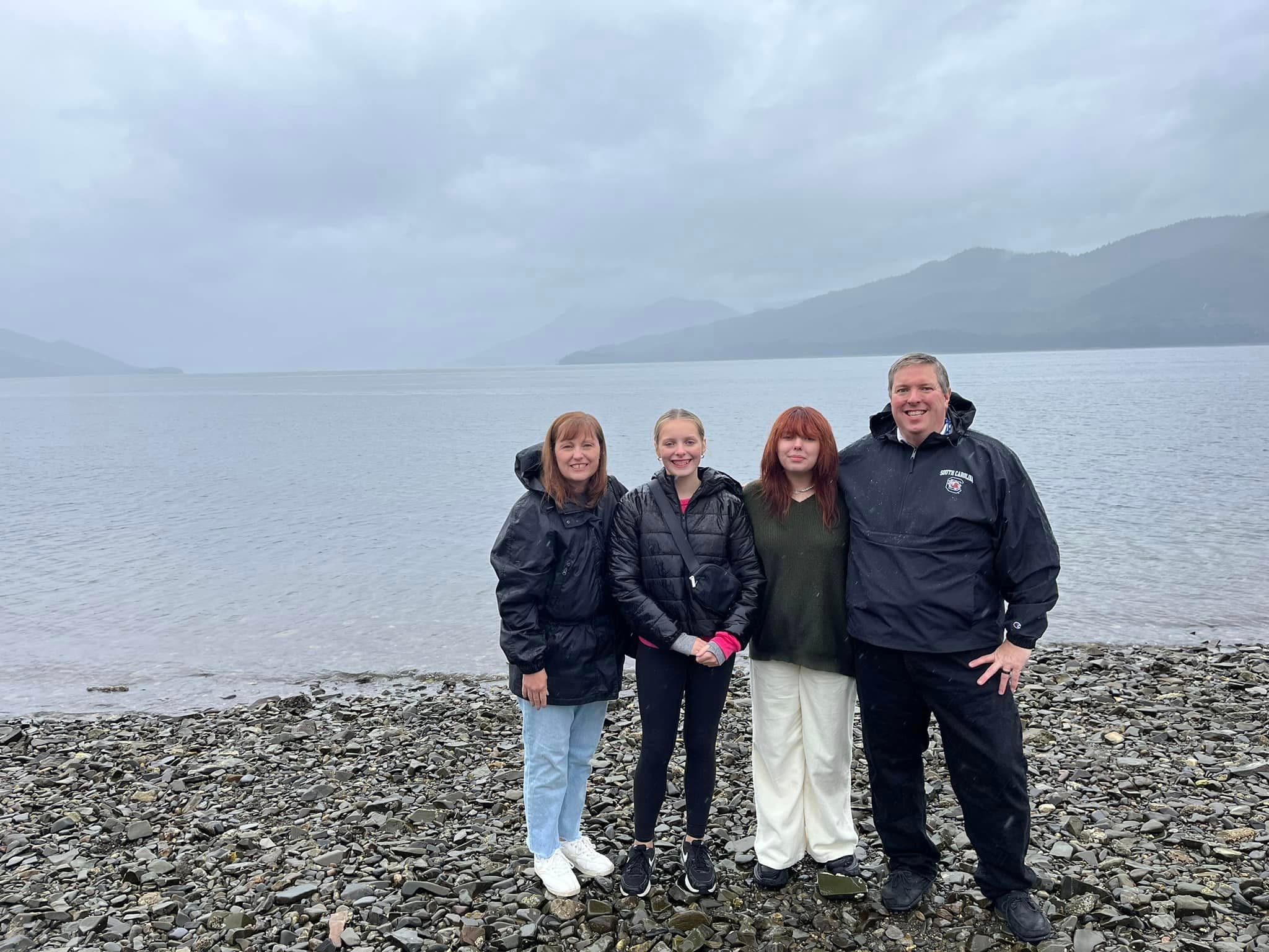 LaTease and her family in winter clothing posing by a large body of water and distant mountains on a foggy day