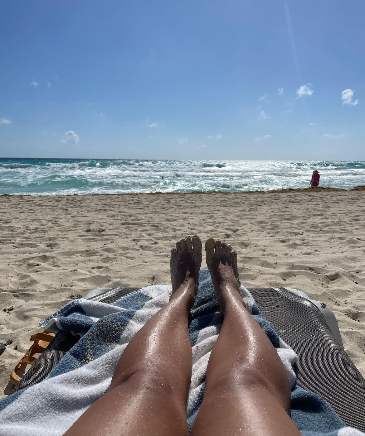 Advisor positions feet on a sandy beach facing the shore on a sunny day. 