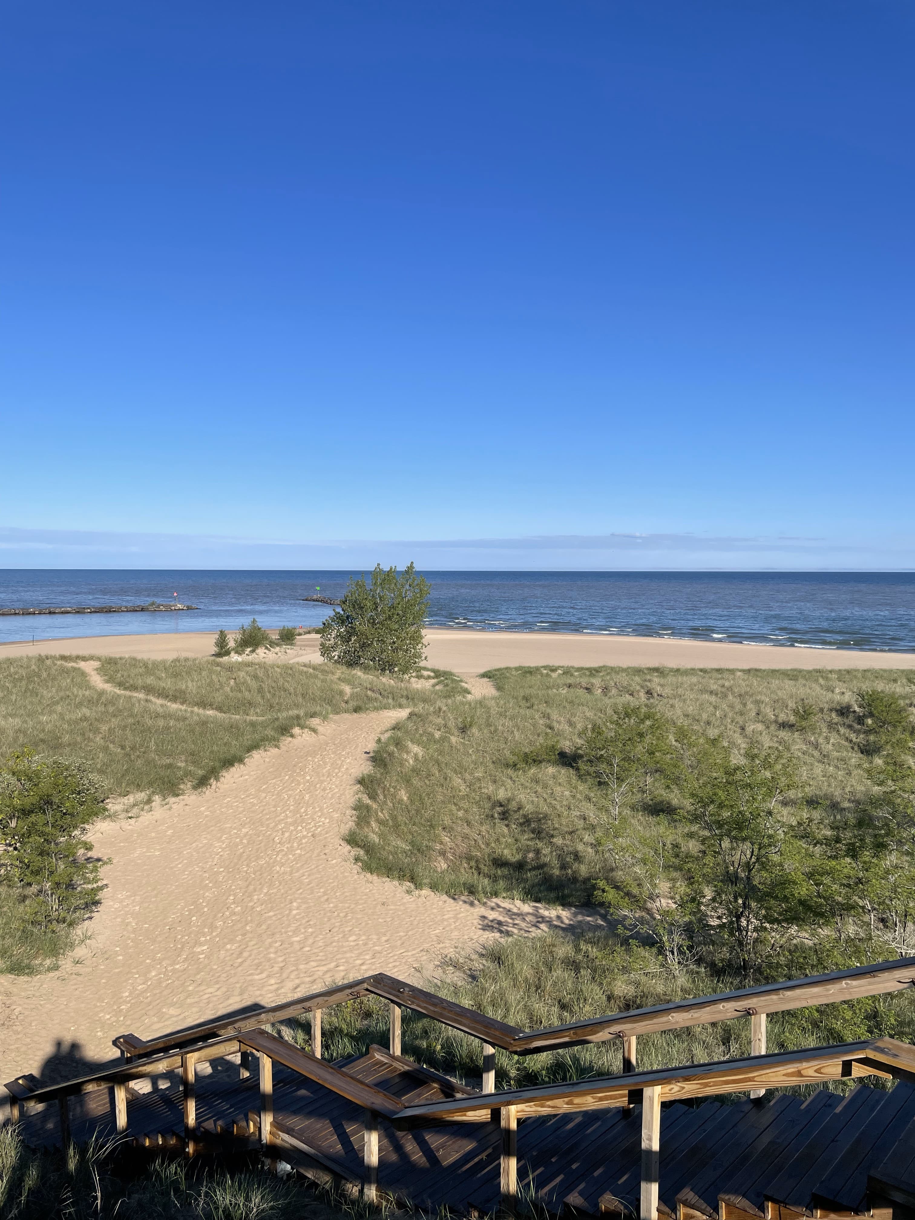 A wooden staircase leading to a sandy pathway and the ocean in the distance under clear skies