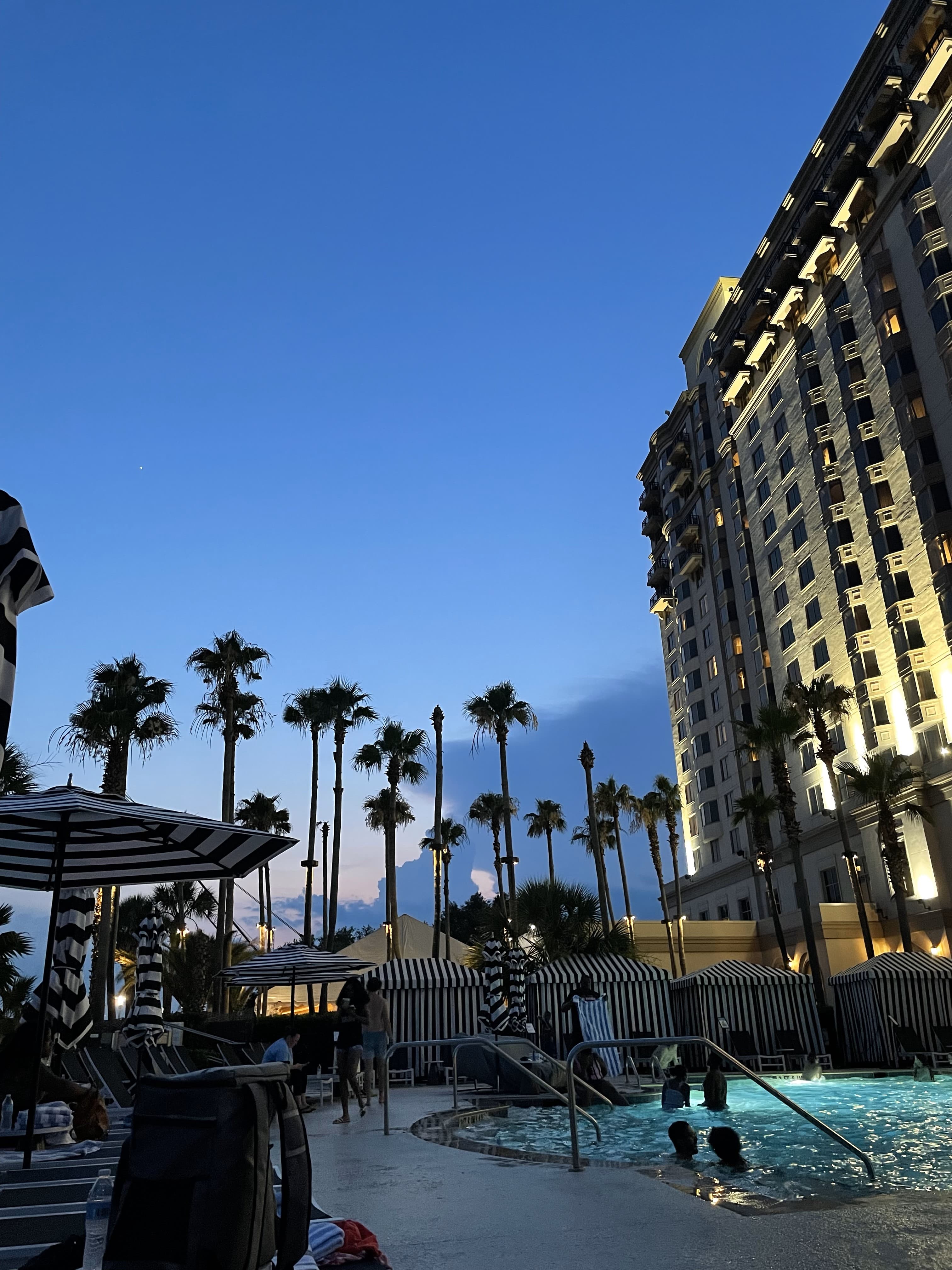 View of a resort pool and large hotel building lit up at dusk