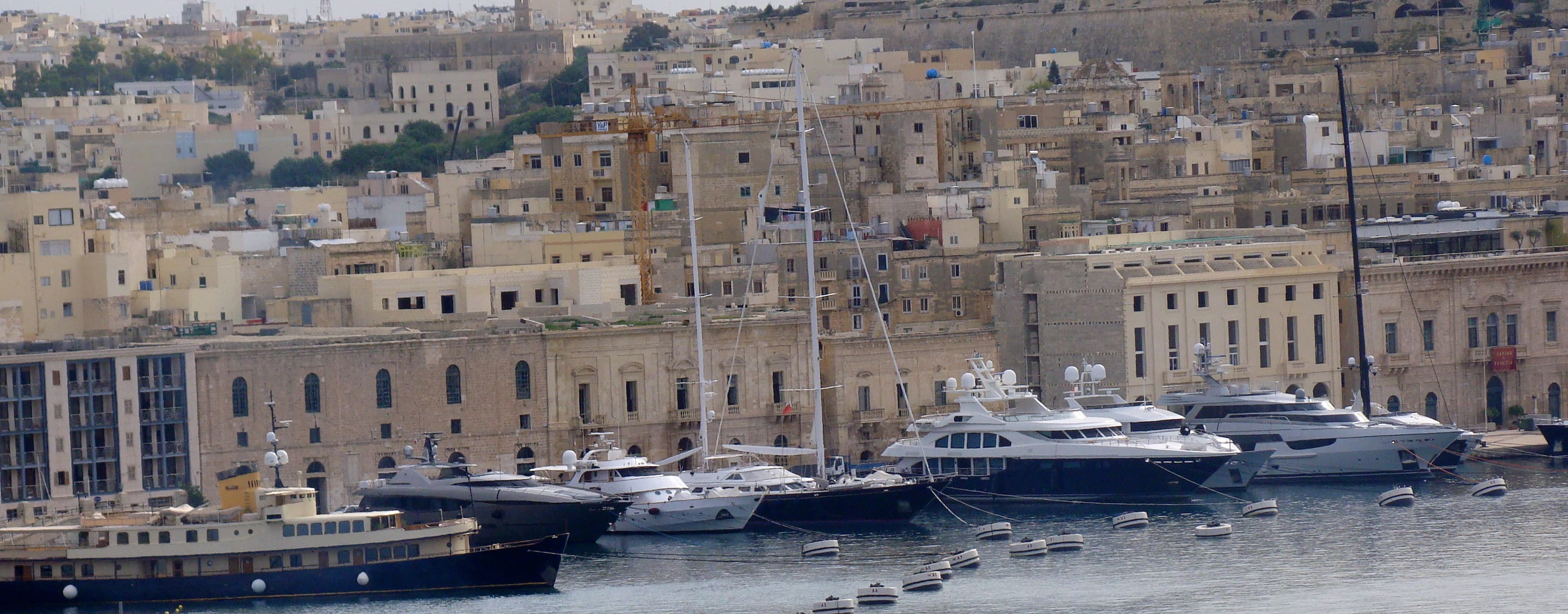 View from the water of several large yachts docked in a port city full of old buildings