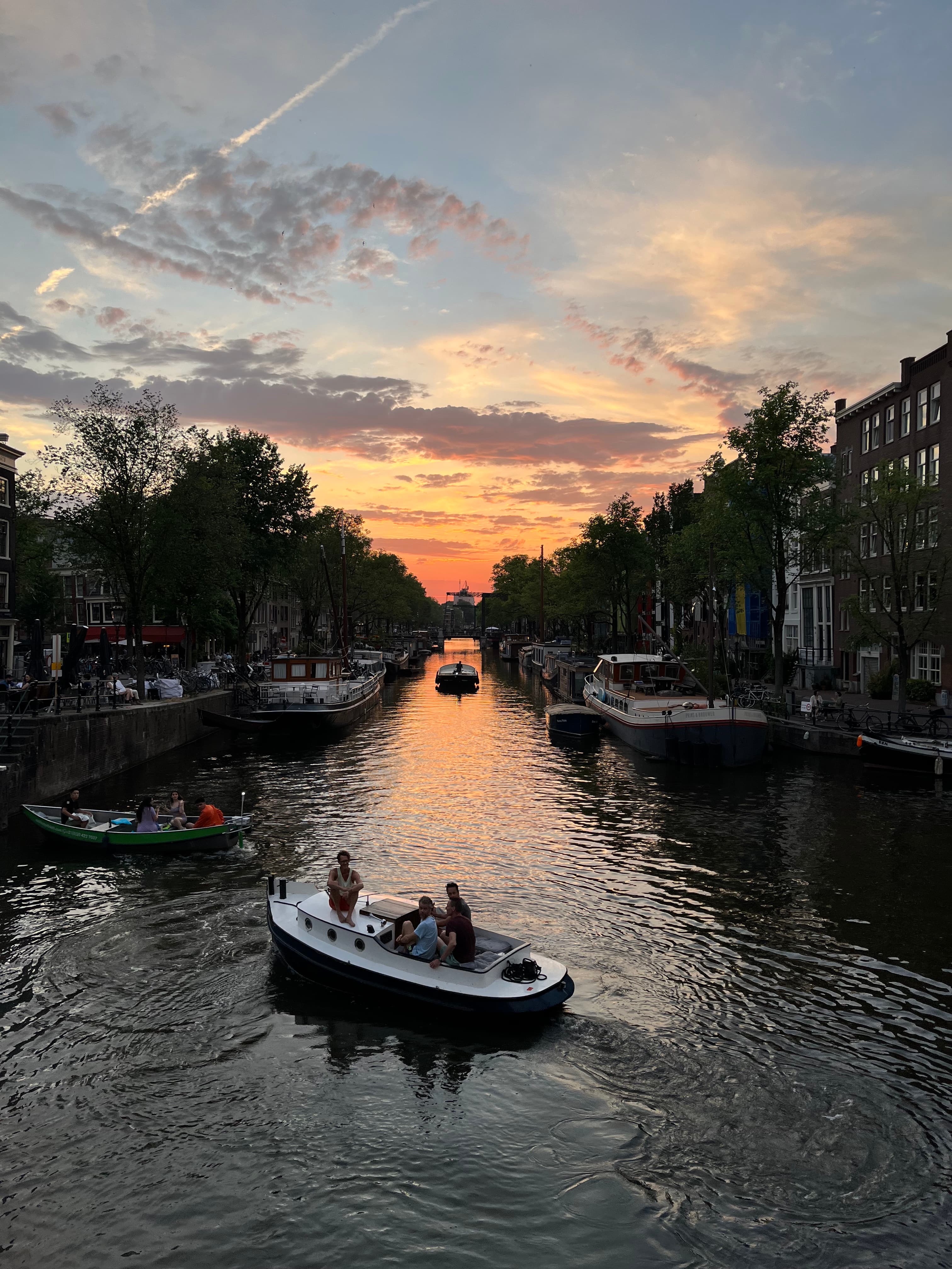 A view of a boat in a canal with foliage in the distance at dusk. 