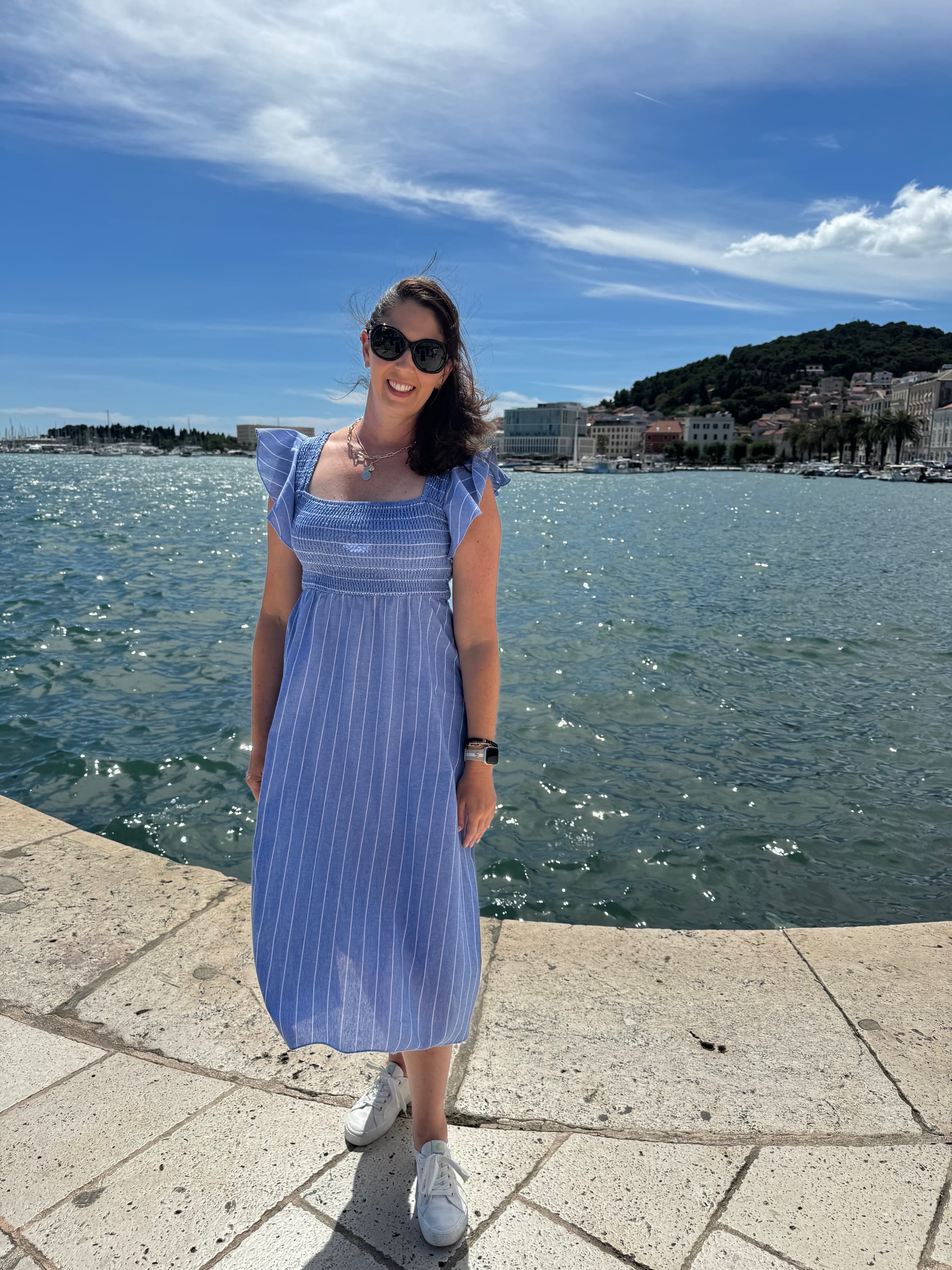 Advisor standing in a blue dress in front of blue calm water and mountains in the distance on a sunny day.