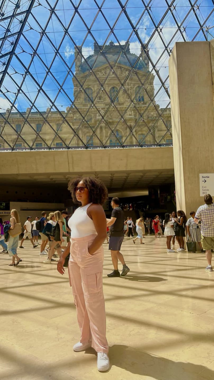 A woman in pink pants and white shirt standing in front of a a building during the daytime.