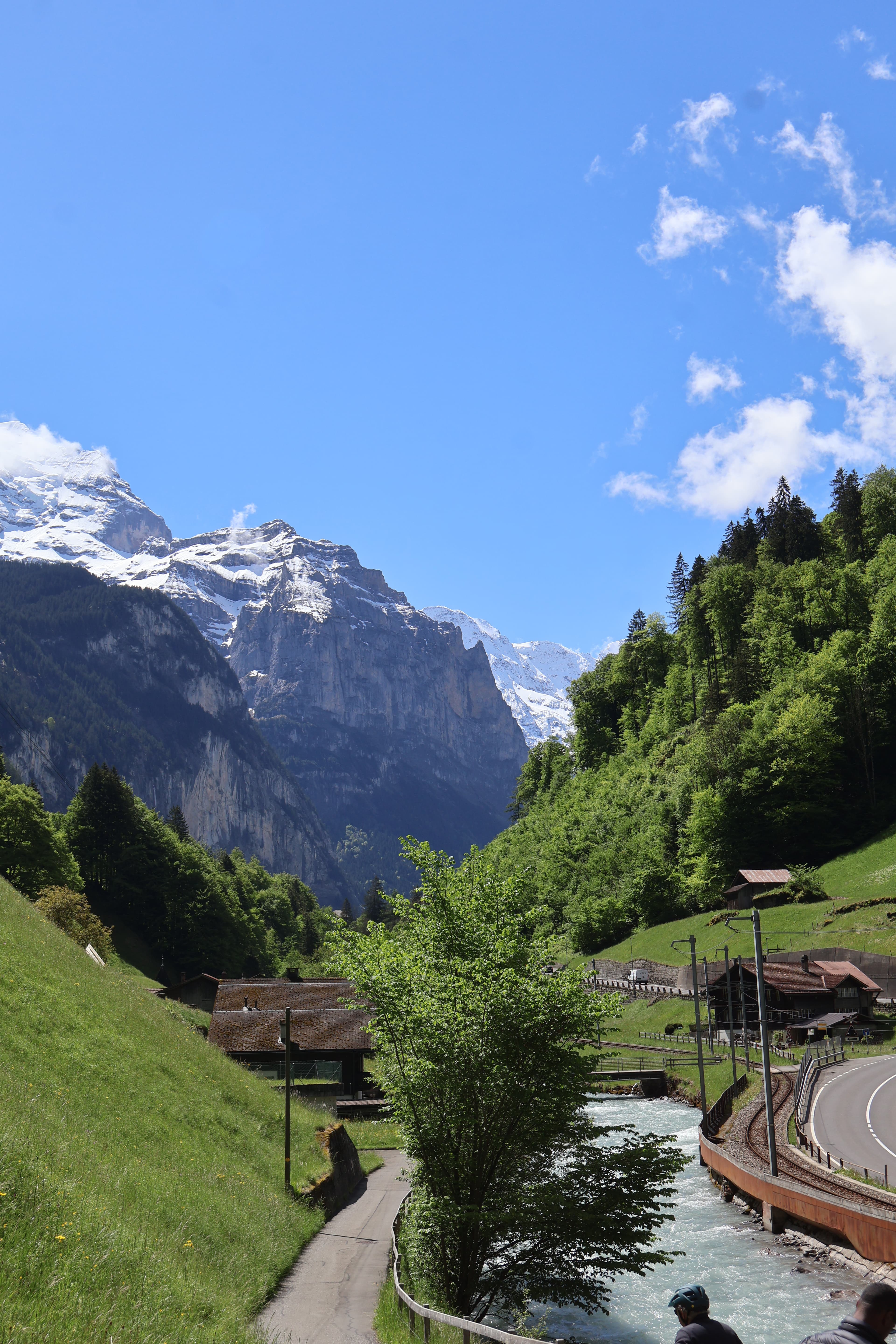 A road winds through a mountainous range covered in dense greenery on a sunny day. 