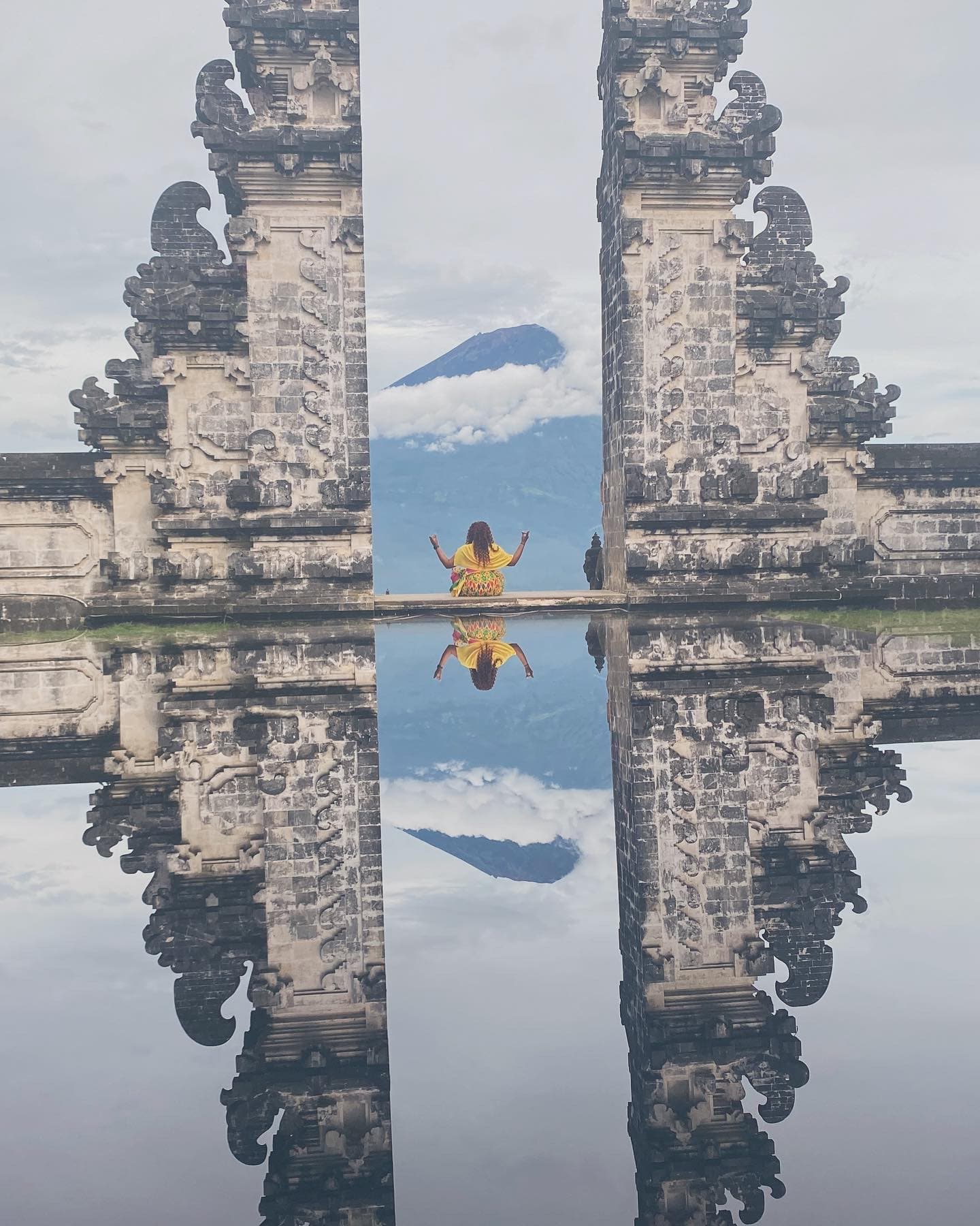  A person sitting on a bench in front of a temple during the daytime.