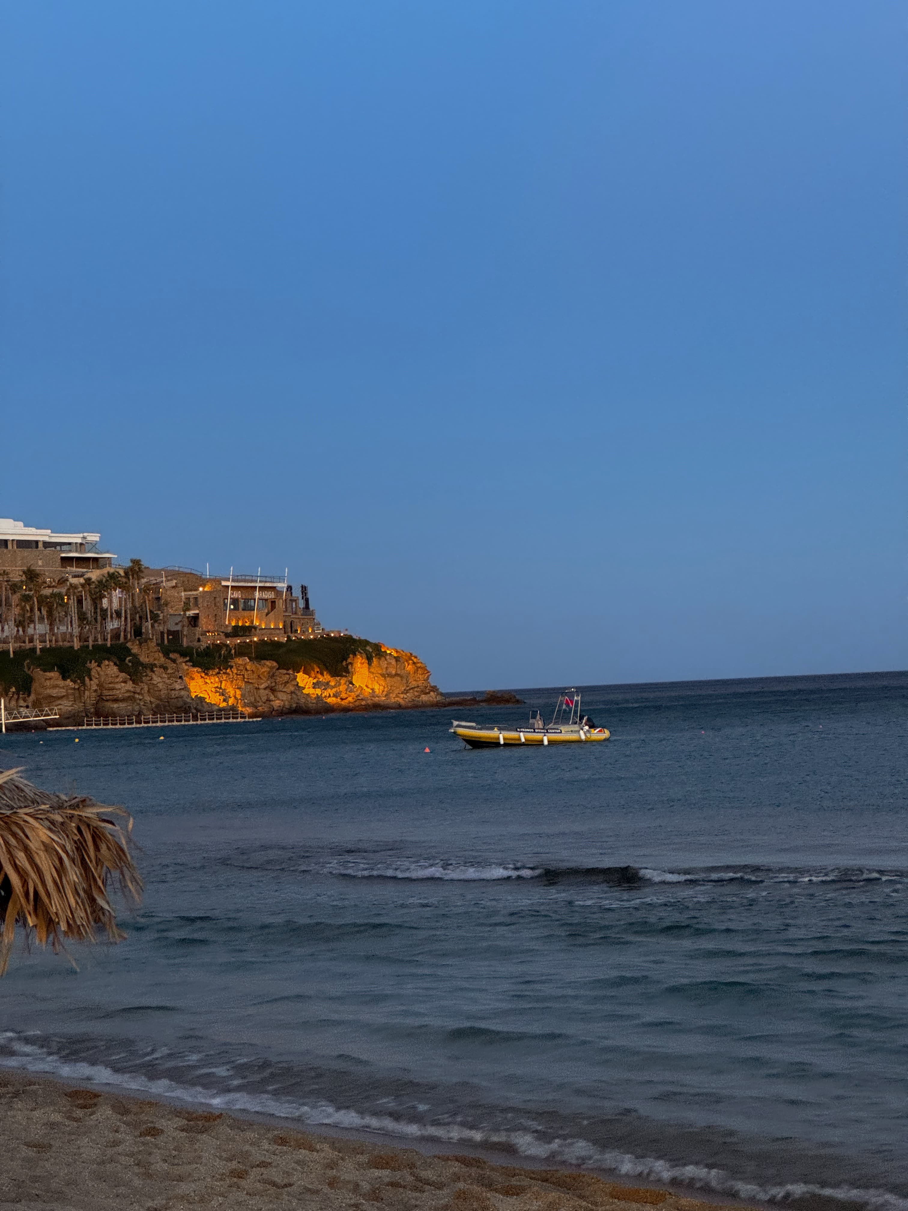 A serene view of a coast line and a boat in the ocean at dusk with cliffs in the distance.   