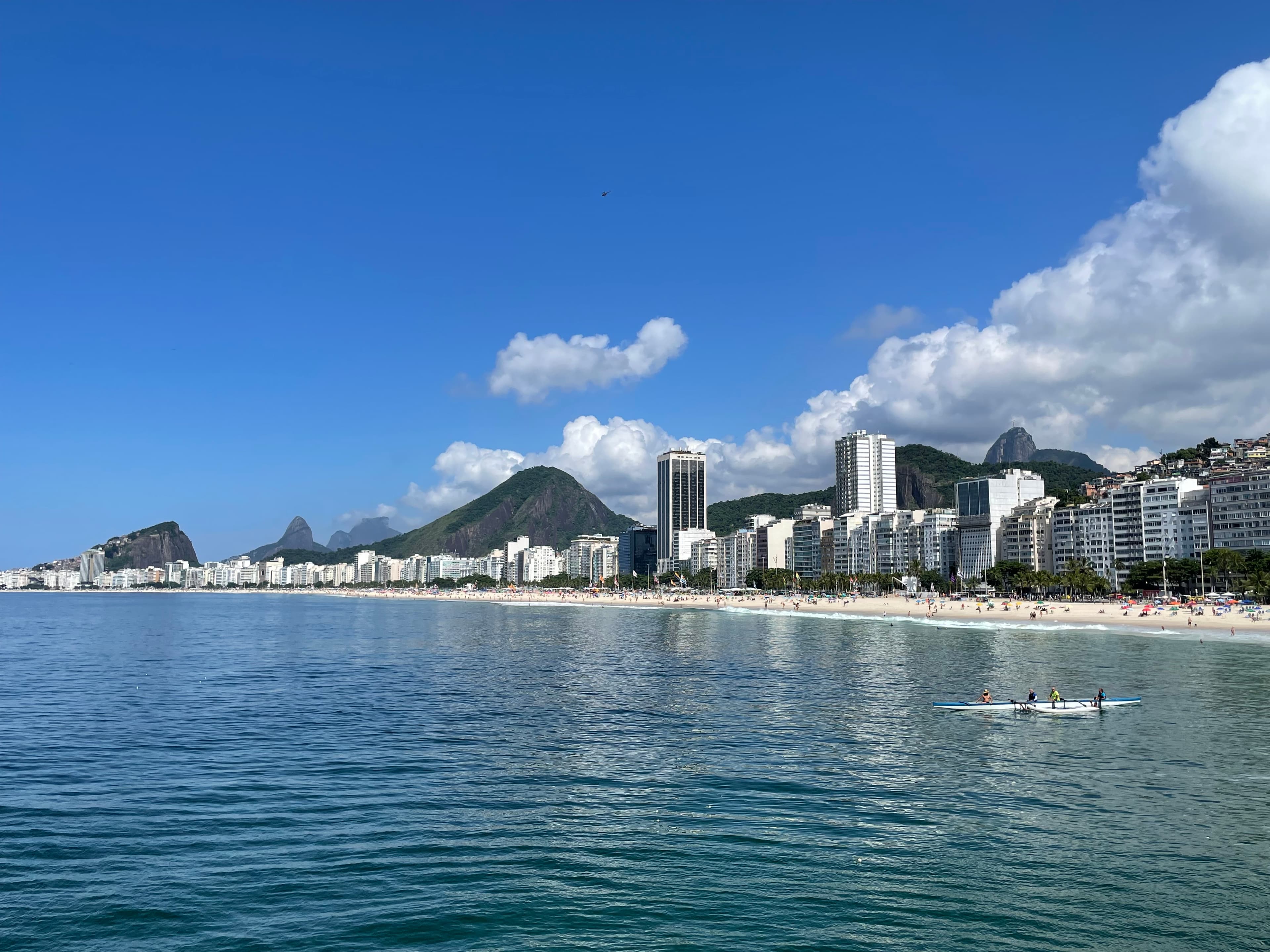 A view of a ocean with a shoreline and a city in the distance on a sunny day.