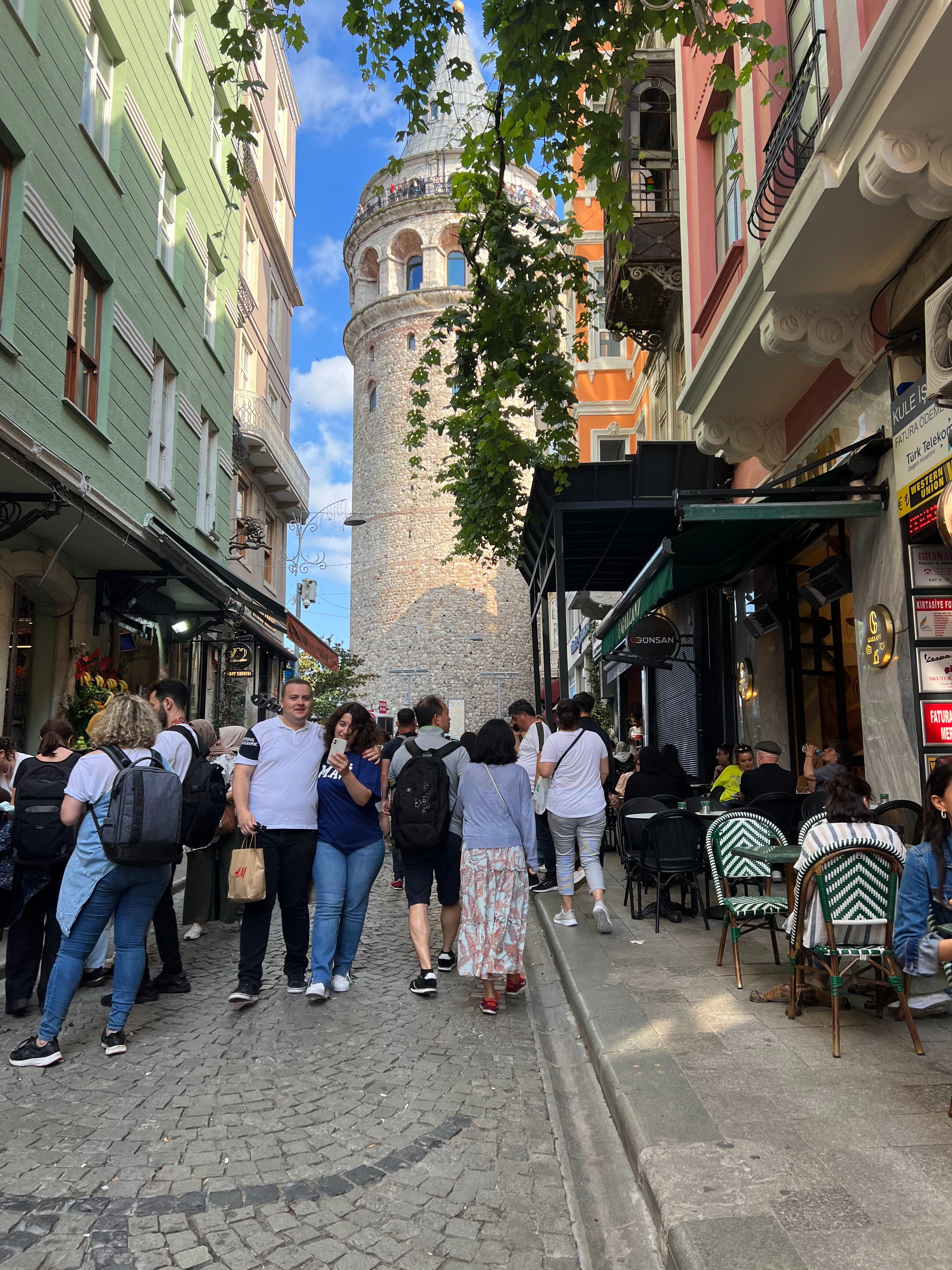 Street scene with people walking and dining near a tower.