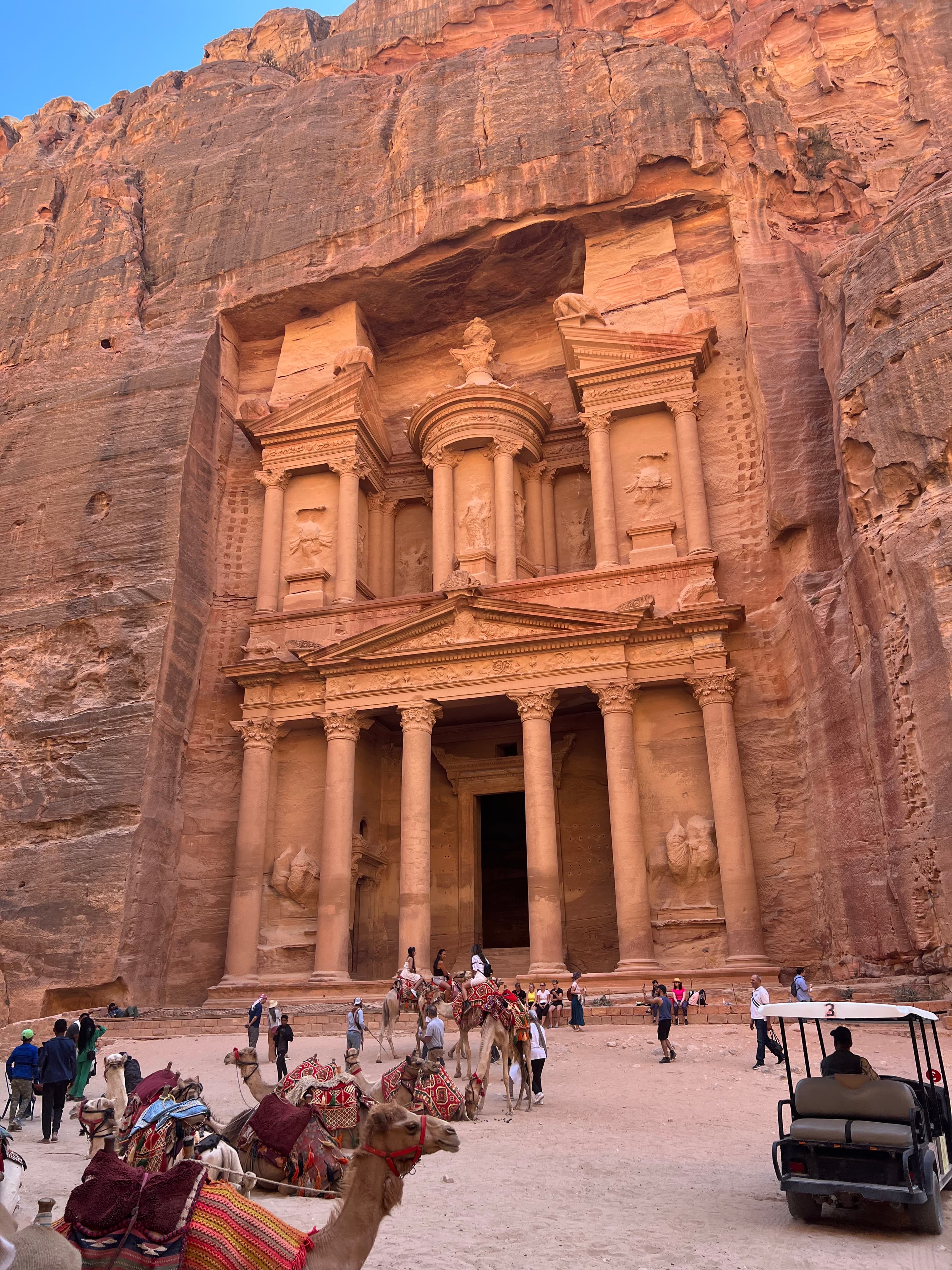 Facade of Al-Khazneh (The Treasury) in Petra, Jordan, with camels and visitors in the foreground.