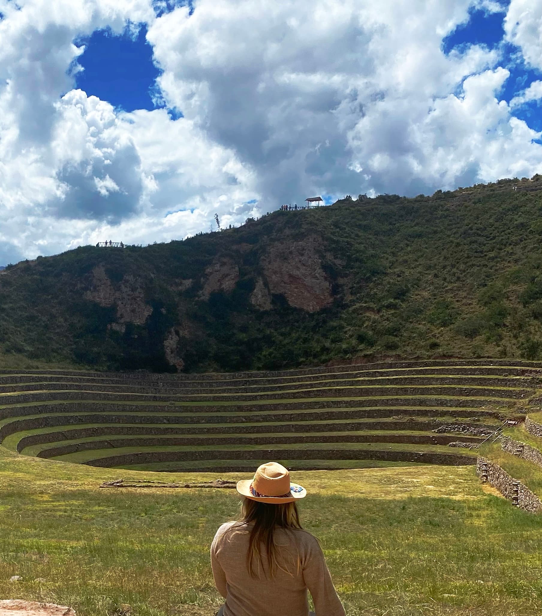 Valeria in a hat overlooking a tiered stadium built into a grassy green landscape 