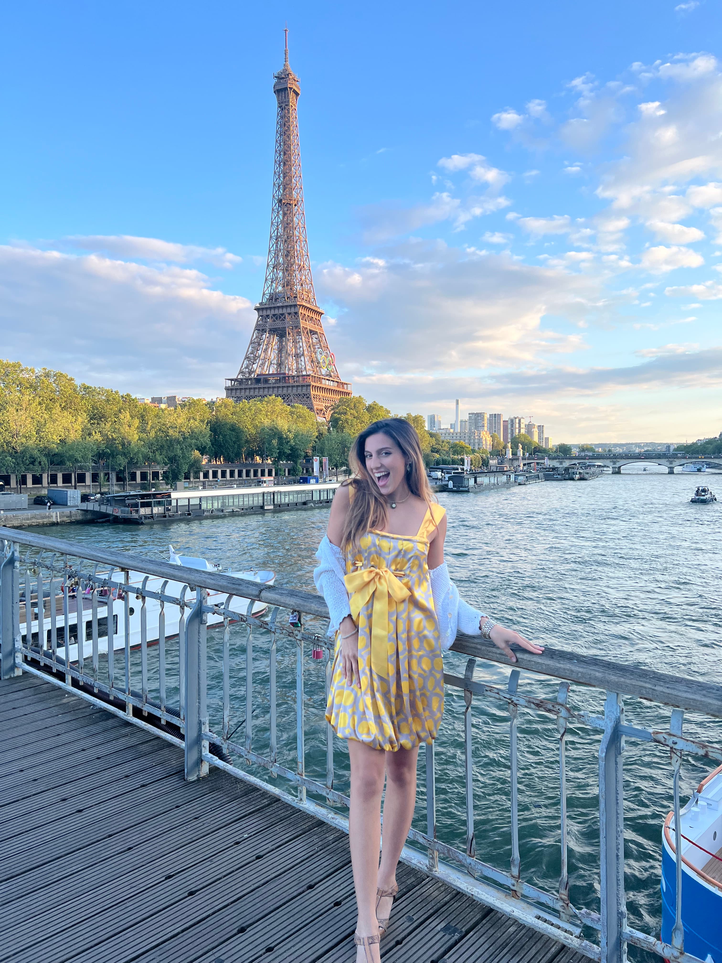 Advisor in a yellow dress leaning against a railing with the Eiffel Tower in the background.