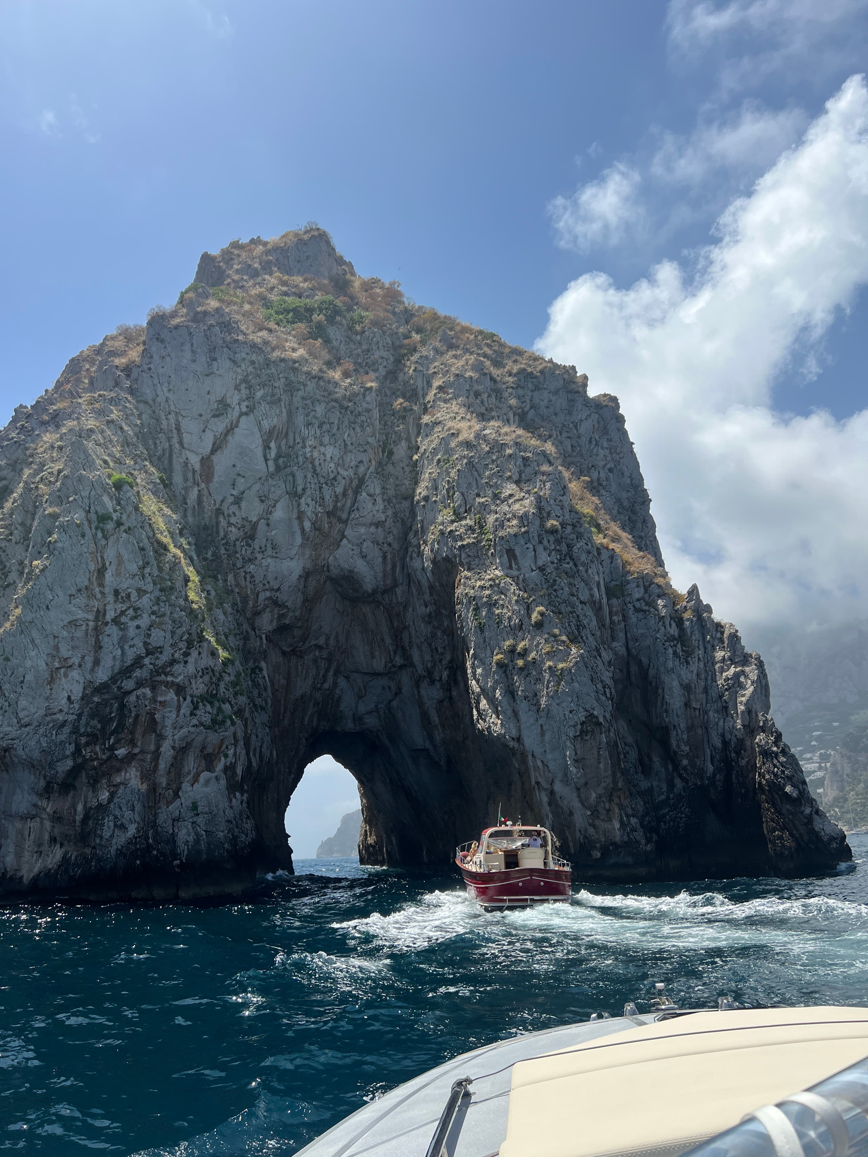 View of a large rock formation at sea seen from a boat with small archway visible in the center 