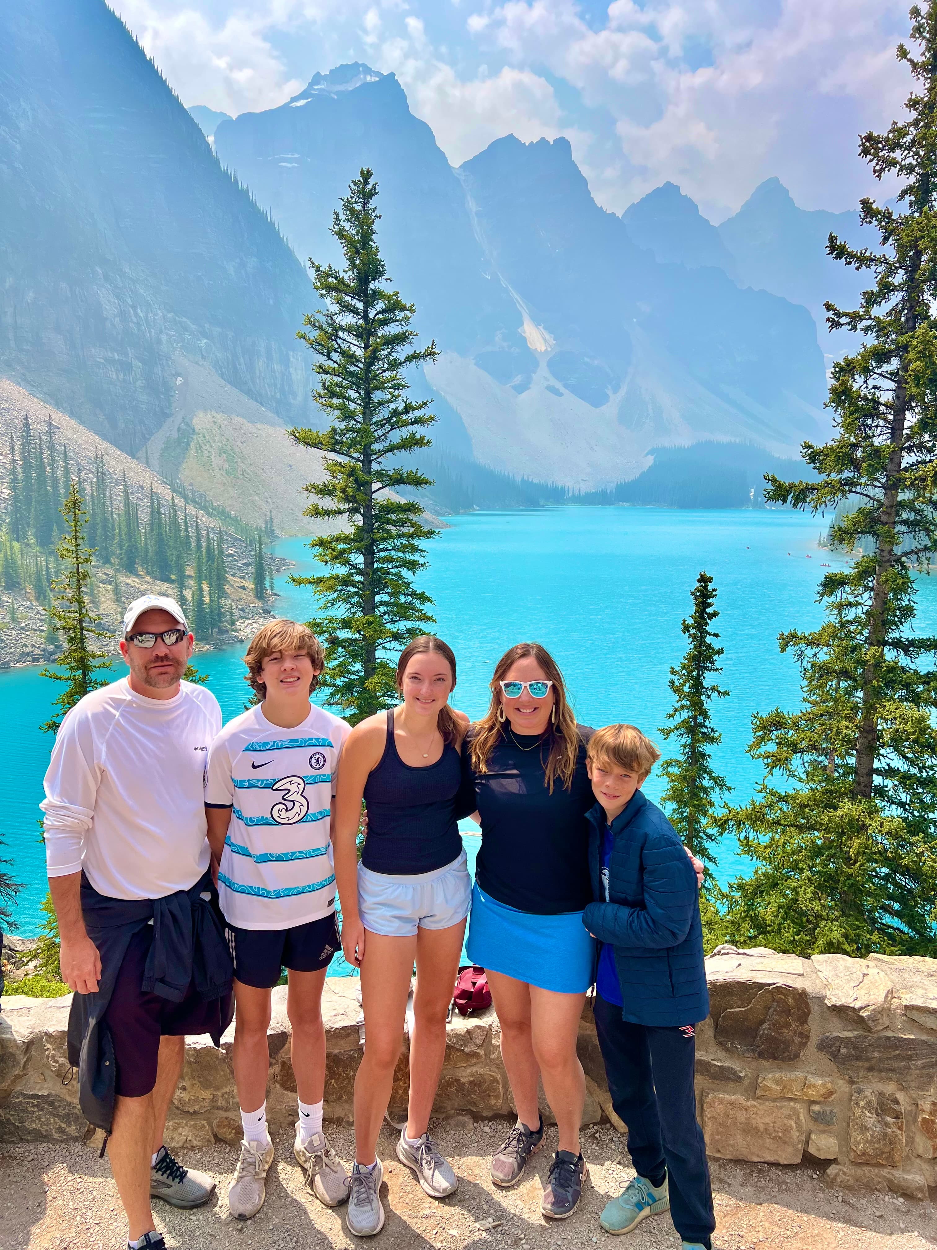 Advisor and her family posing at a lookout point in front of a beautiful bright blue lake surrounded by mountains