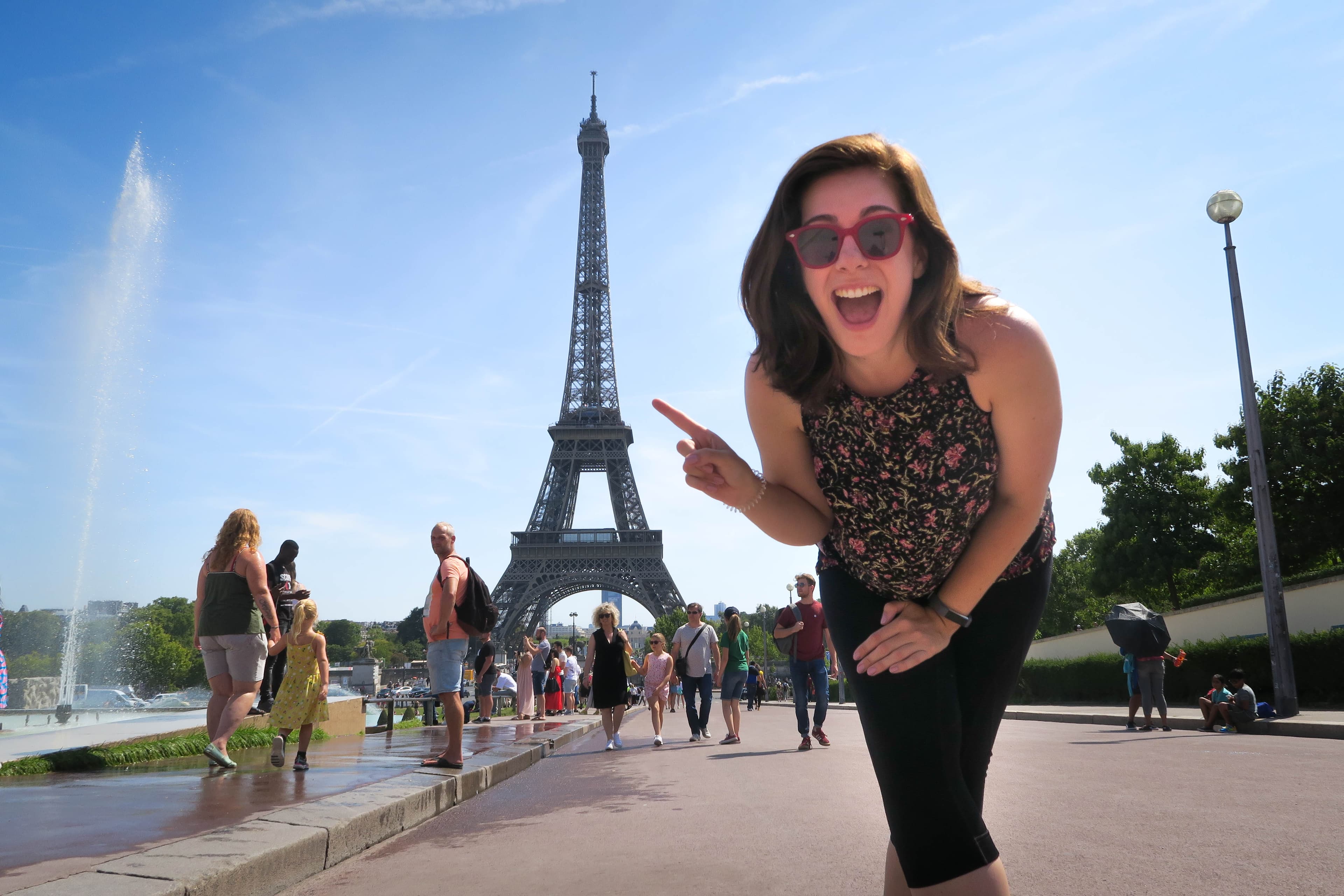 Advisor posing in front of the Eiffel Tower with her finer pointing towards it on a sunny day