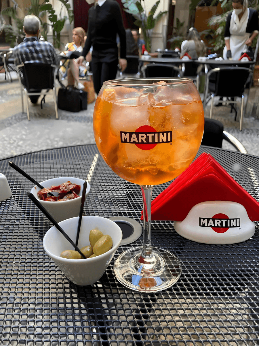 View of a large Aperol spritz and snacks on an outdoor table on a sunny day