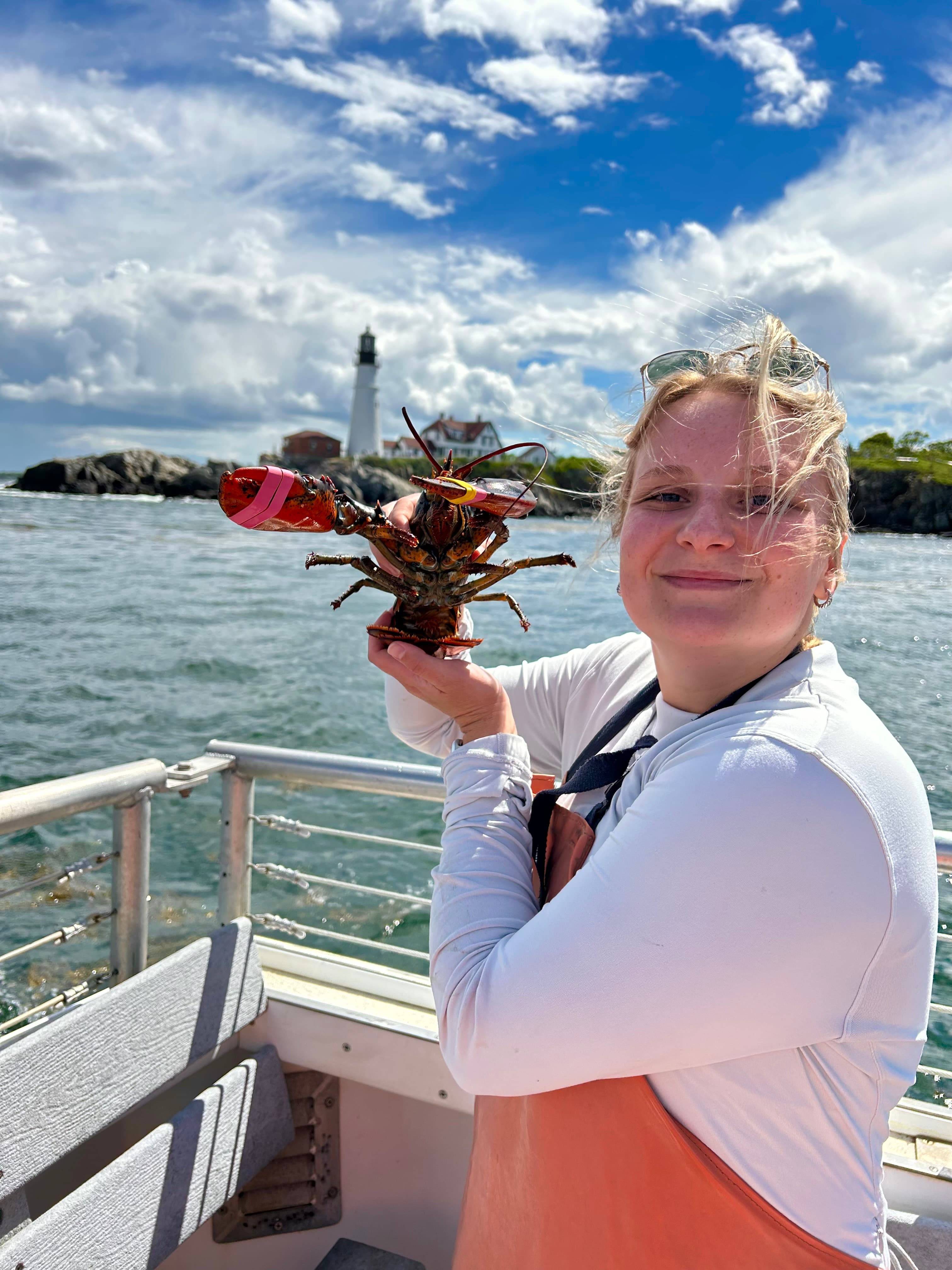 Advisor posing hold a lobster in her hand with the ocean in the background.