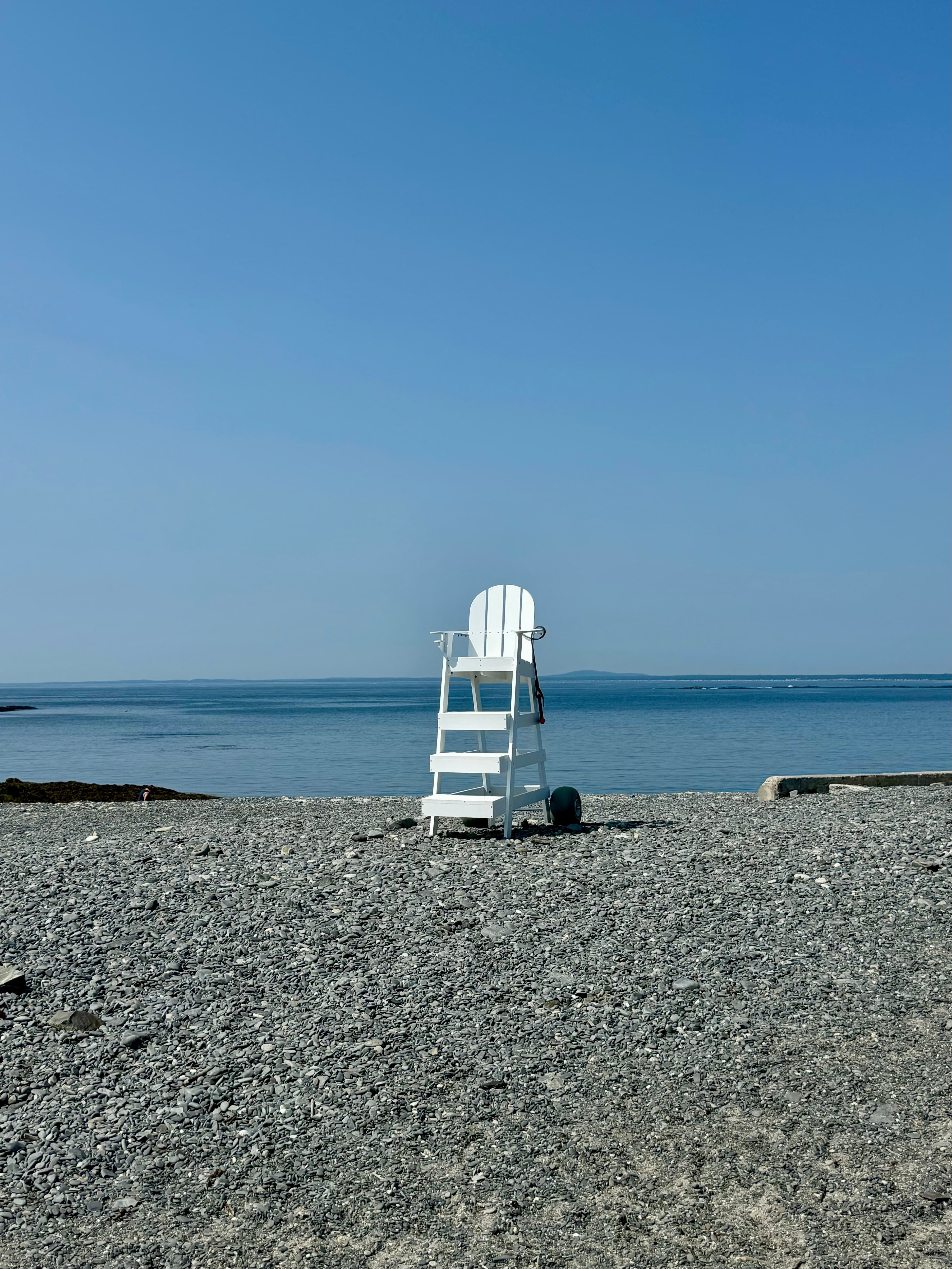 A lifeguard chair on a beach with the ocean in the distance on a sunny day. 