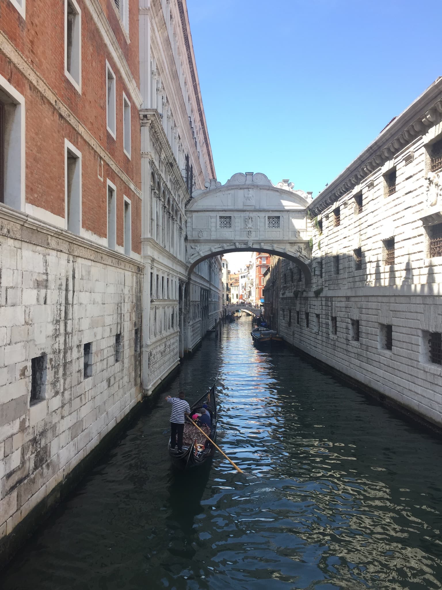 View of a canal in Venice, Italy with a sole gondolier steering a boat on a sunny afternoon