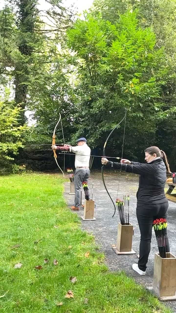 Leslie and a man shooting a bow and arrow outdoors