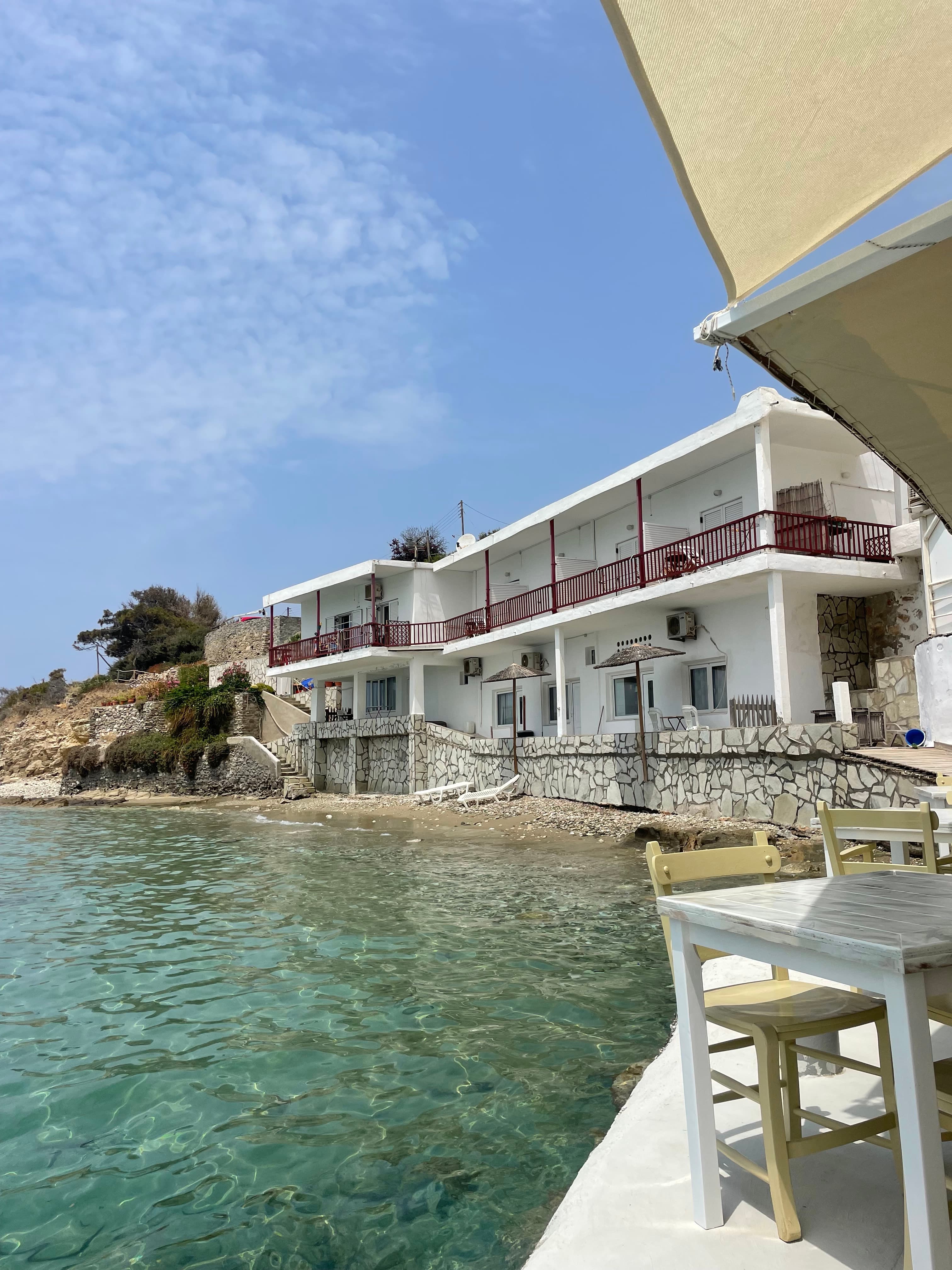 View of an outdoor table on a platform beside the sea and a small while building behind it
