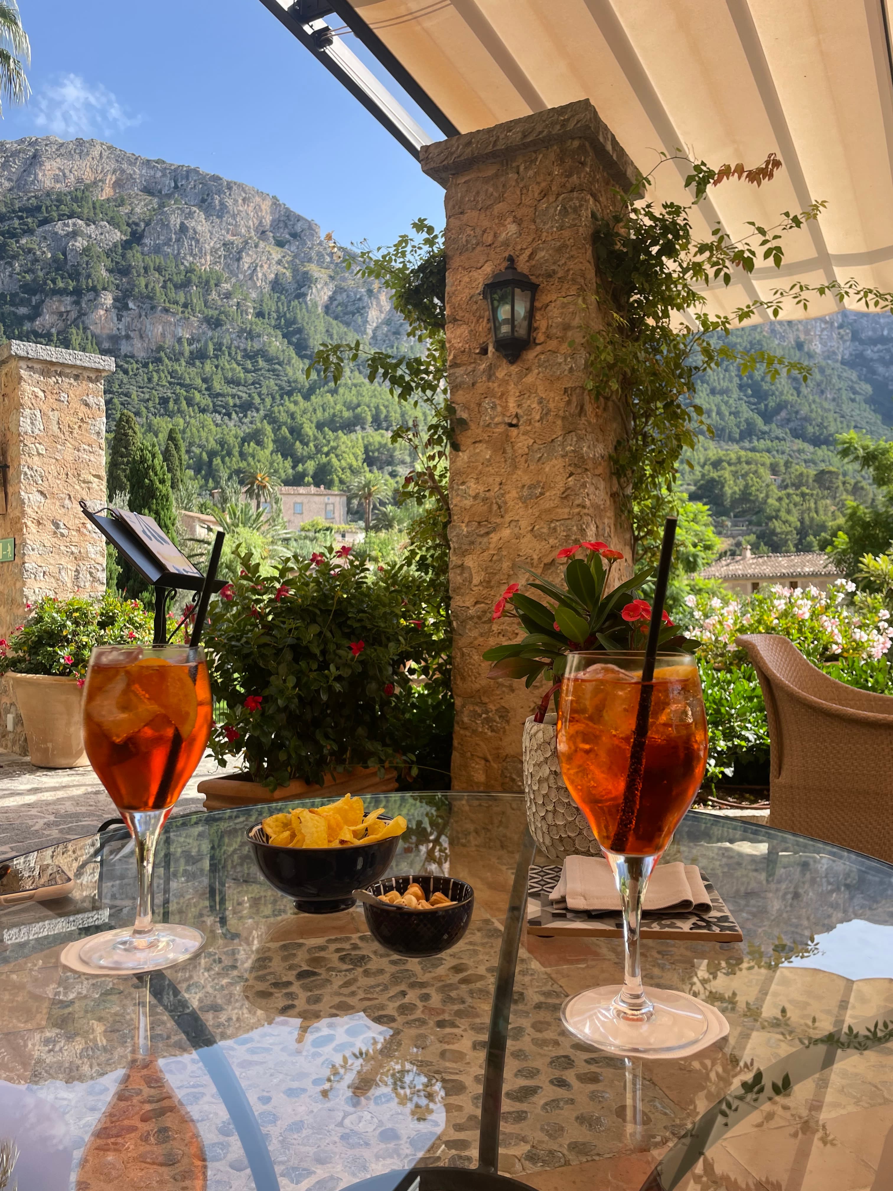 View of two Aperol spritzes on an outdoor table and beautiful mountains visible in the background
