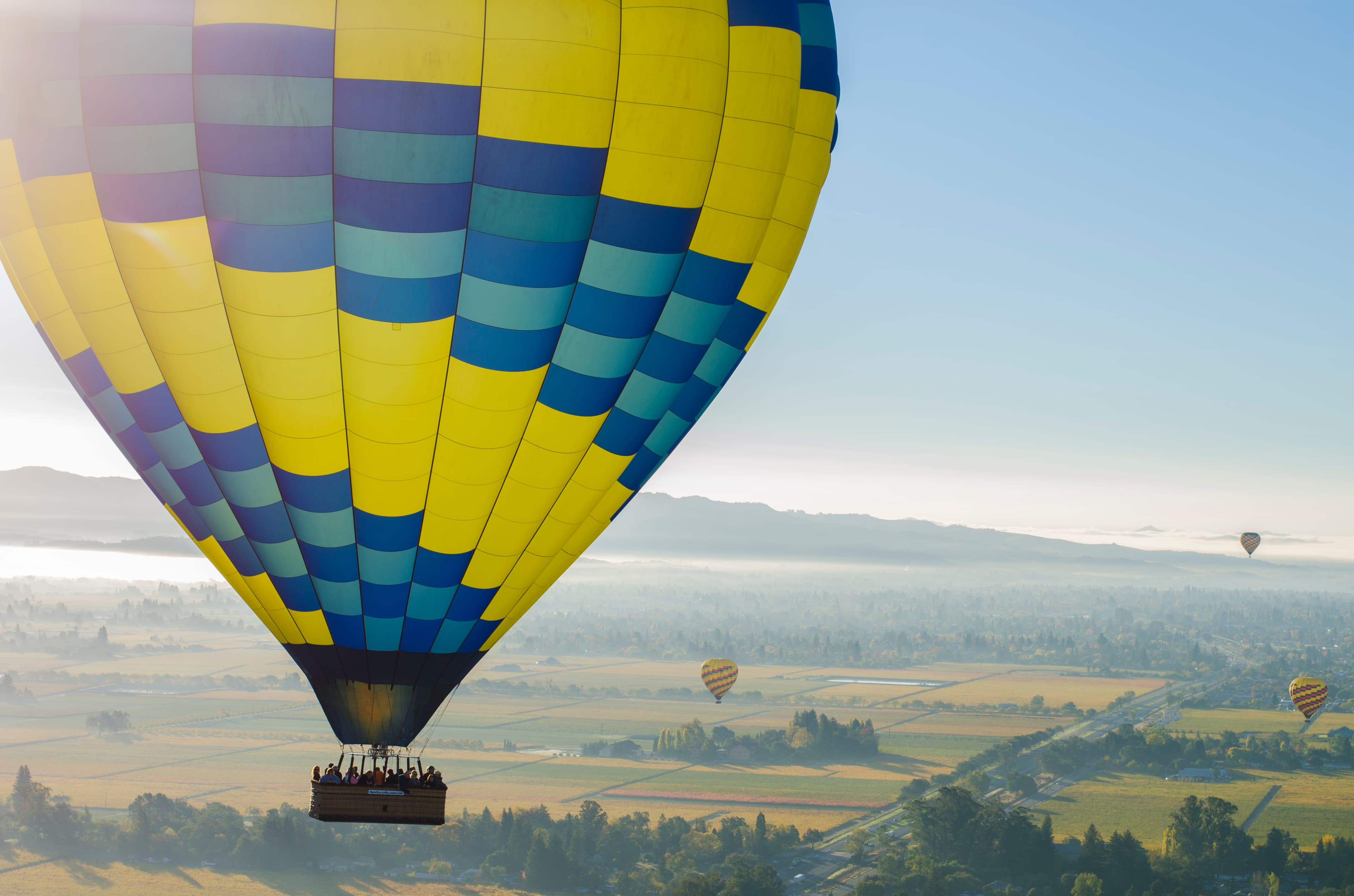 View of a yellow and blue hot air Mallon in the sky overlooking a beautiful green landscape