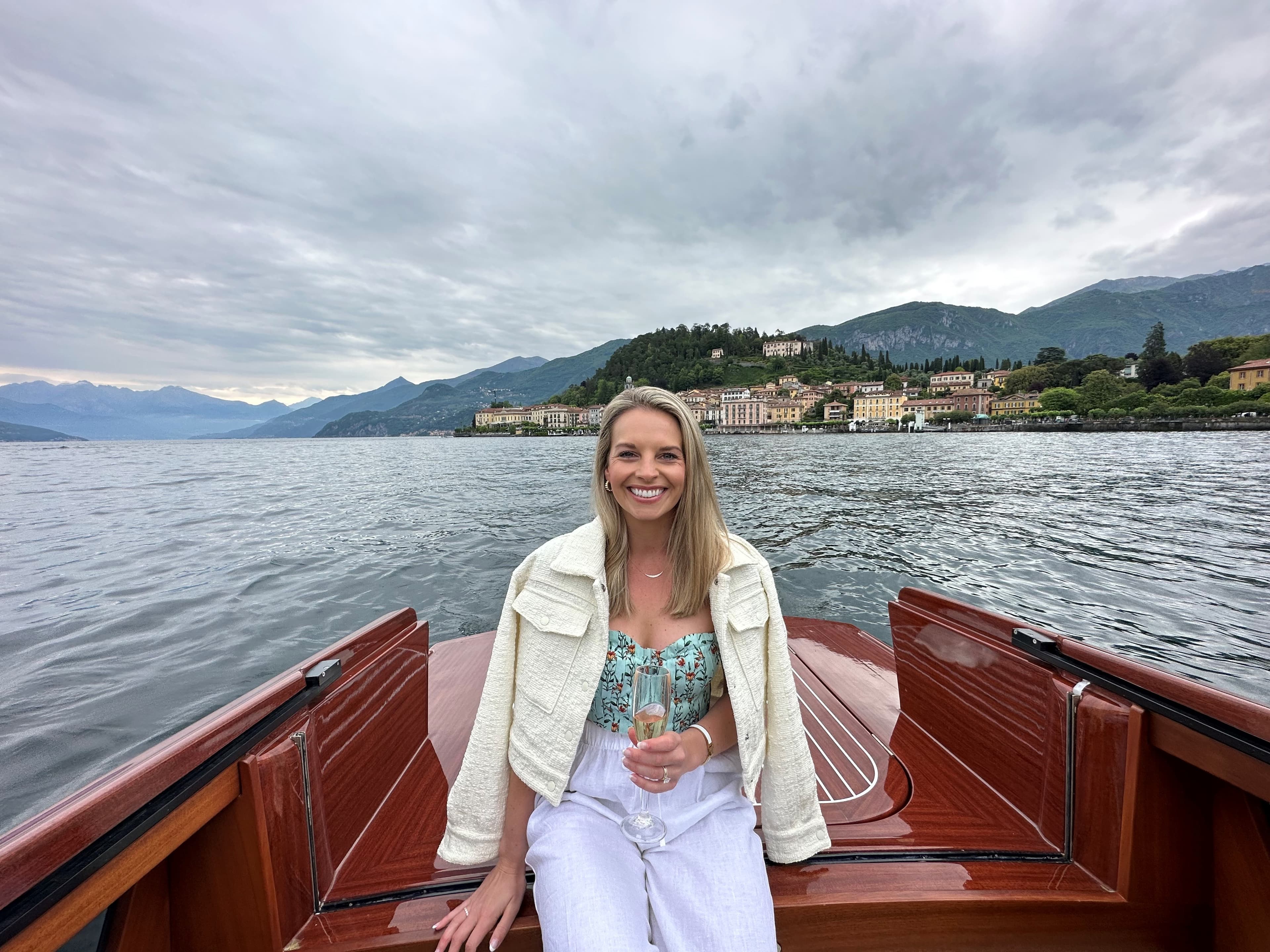 Advisor in white pants and a jacket seated on the back of a boat on Lake Como under cloudy skies
