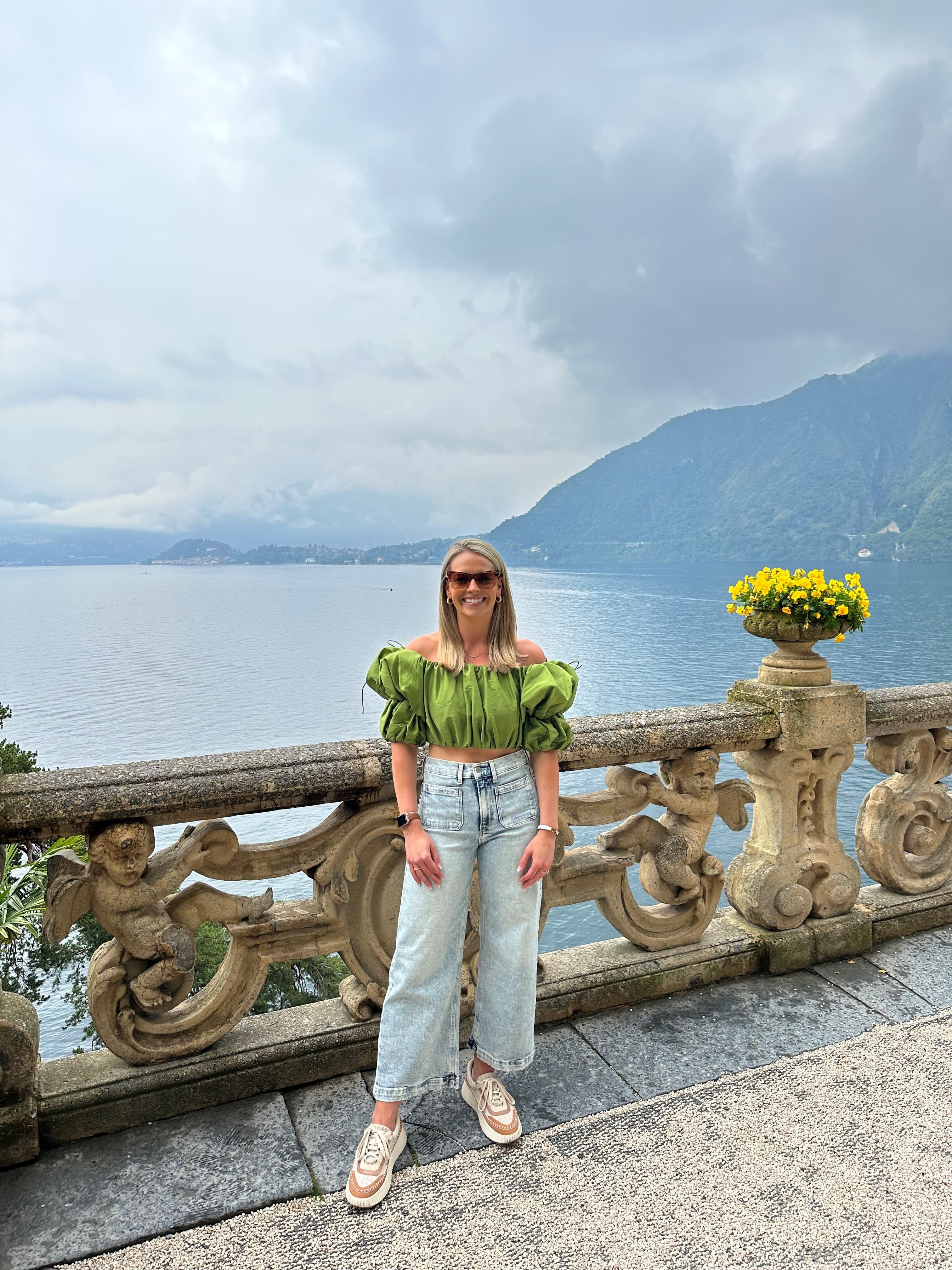 Advisor in a green top and sunglasses posing by a large lake surrounded by mountains