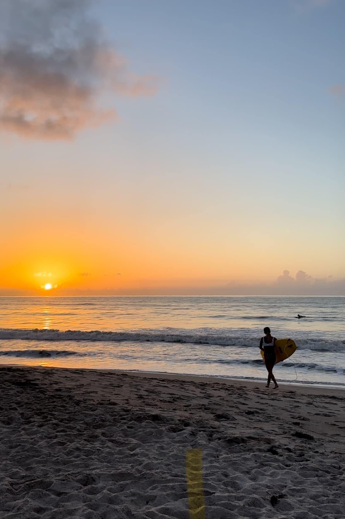 Beautiful view of a person holding a surfboard walking along an empty beach at sunset